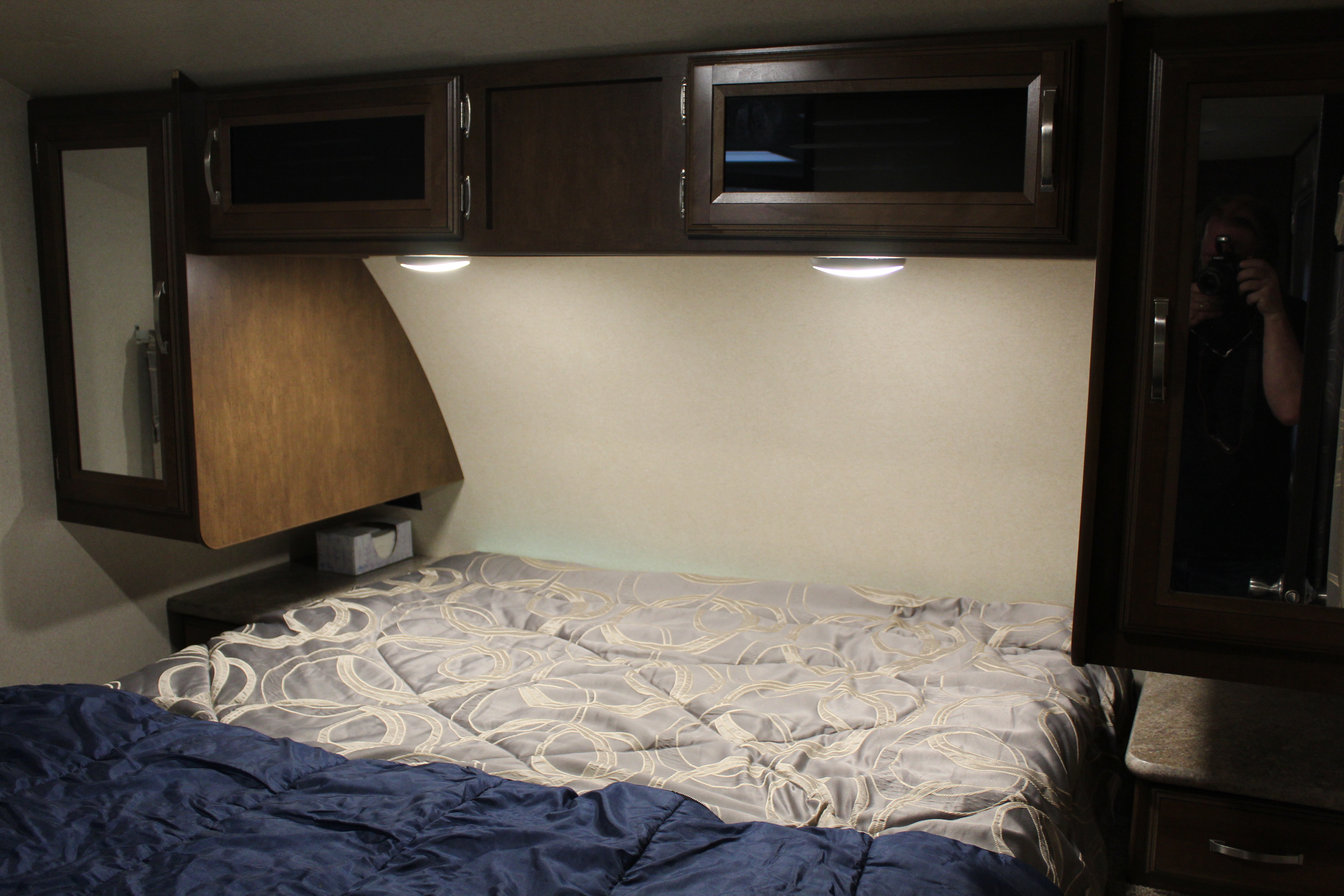 Inside an RV rental: a cozy bedroom with a patterned comforter on the bed, overhead cabinets, and reading lights.. Forest River Salem Hemisphere Hyper-Lyte 2017