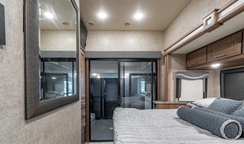 Spacious RV rental interior featuring a cozy bed, mirror, and sliding door leading to a separate garage area.. Thor Motor Coach Outlaw 2022