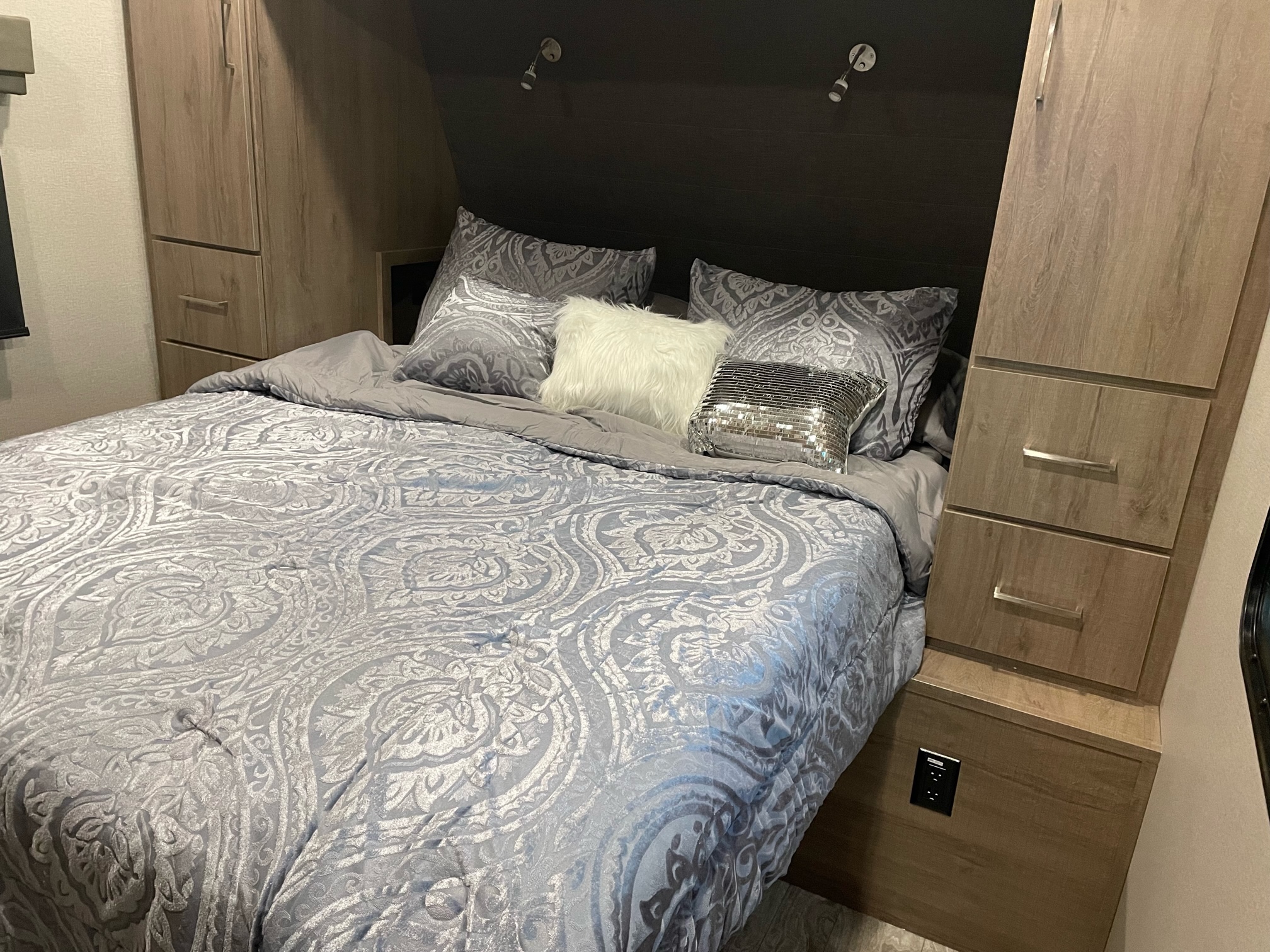 Cozy RV rental bedroom with a large bed, grey patterned bedding, decorative pillows, built-in wooden cabinets, and reading lights.. Grand Design Imagine RL 3100 2022