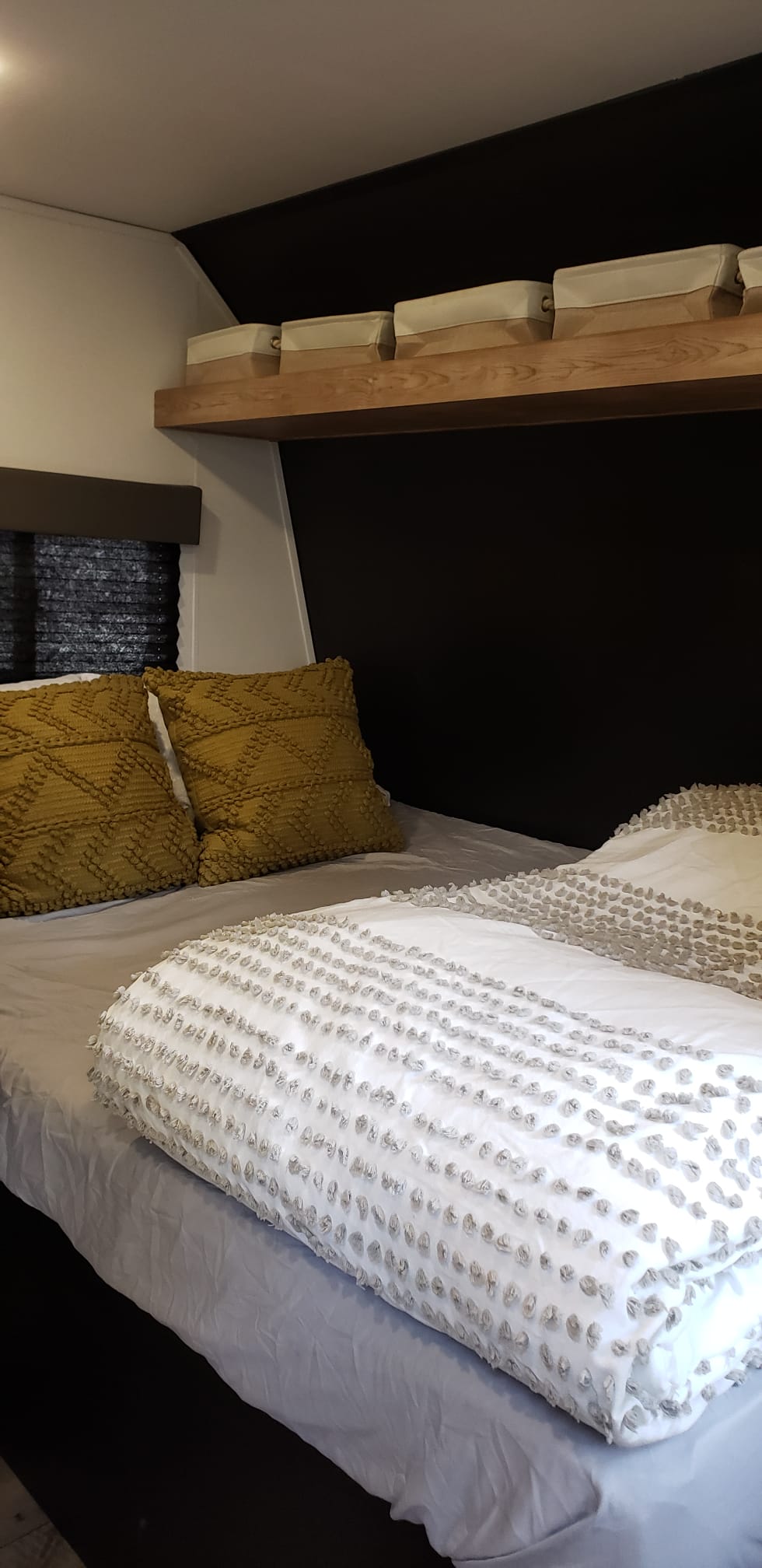 Modern RV rental bedroom: comfy bed with textured white bedding, yellow pillows, & storage shelf.. Keystone RV Springdale 2022