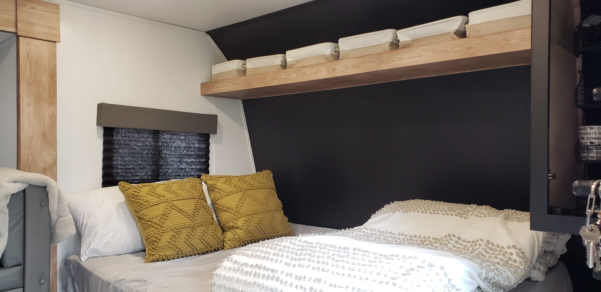 Cozy RV rental bedroom with a dark accent wall, wood shelf, and comfy bed with yellow pillows and storage.. Keystone RV Springdale 2022