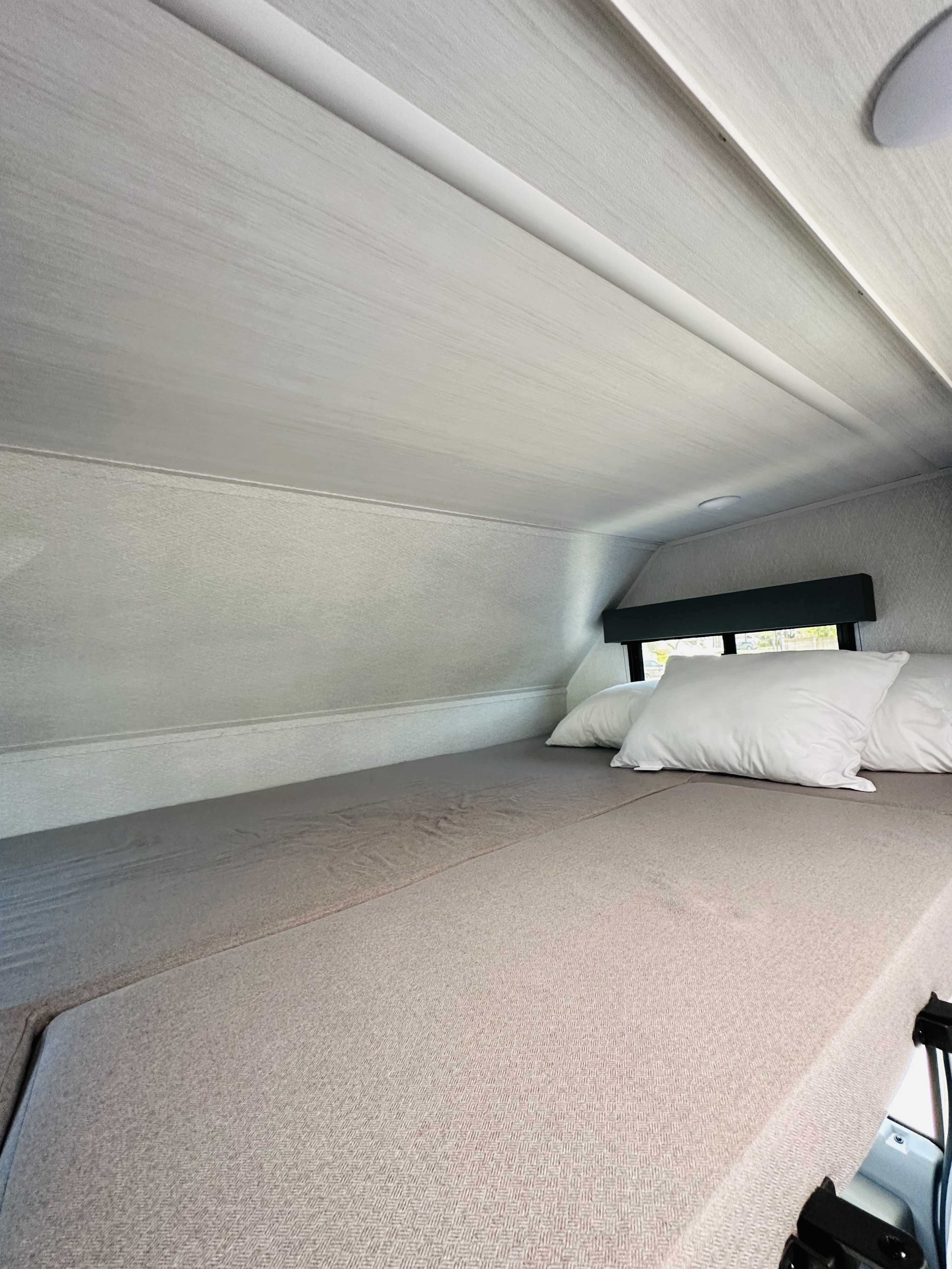 Cozy RV rental interior featuring a comfy bed with white pillows and a window, ideal for restful travels.. East to West Entrada 2023
