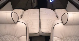 This RV rental interior shows plush white seats and two quilted beds ready for comfortable sleep. Perfect for travel comfort.. Midwest Automotive Designs Ultimate Coach 2022