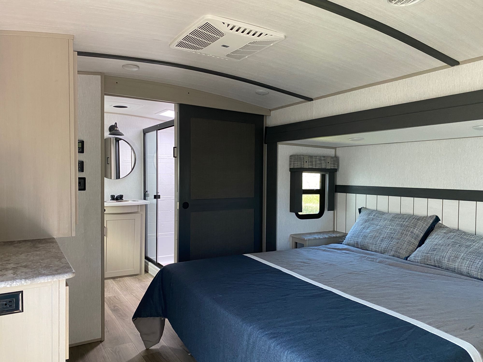 An RV rental's modern interior: a cozy bedroom with a queen bed, connecting to a full bathroom with a vanity and shower.. Forest River Heritage Glen Elite 2023