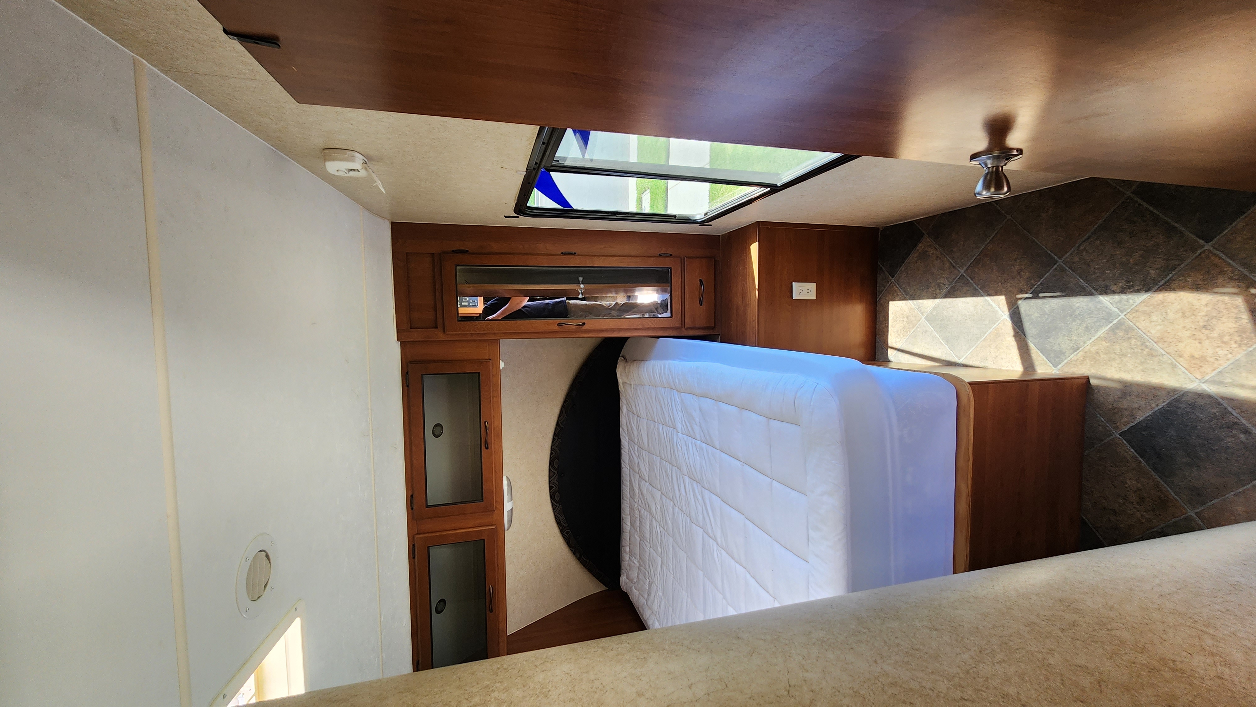 Inside an RV rental: a bright bedroom with a white mattress, wooden cabinets, and a large overhead skylight.. Pacific Coachworks Powerlite 2014