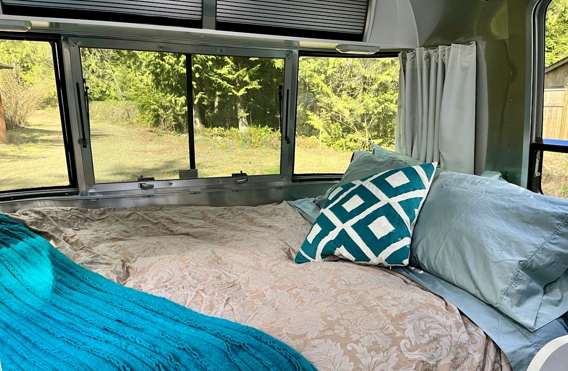 Relax in this RV rental bedroom: A comfortable bed with patterned bedding and blue pillows overlooks a serene natural view.. Airstream Sport 2019