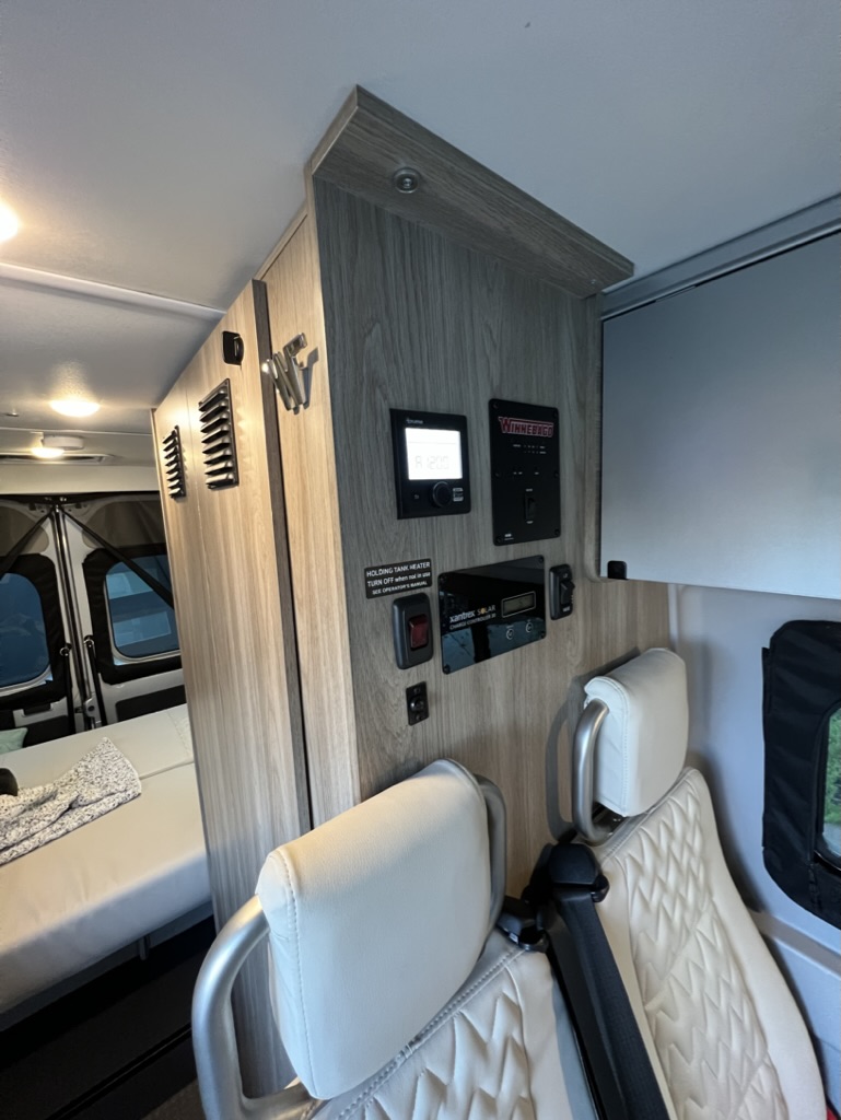 RV rental: Interior showing control panel, two light-colored seats, and a bed. Essential camper systems visible.. Winnebago Solis 2022