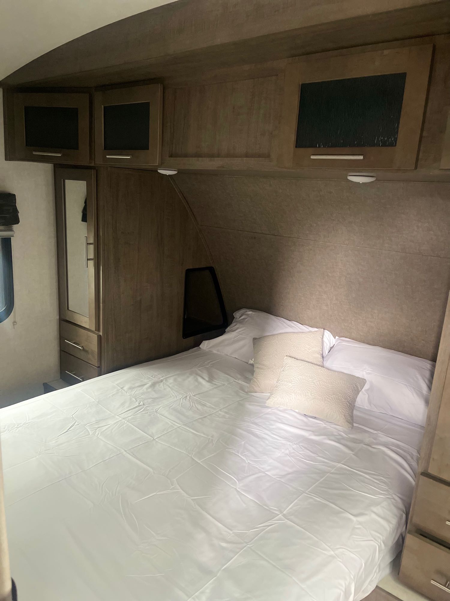 Cozy RV rental bedroom featuring a bed with white linen, ample overhead storage, and a mirrored wardrobe.. Forest River Surveyor 2018