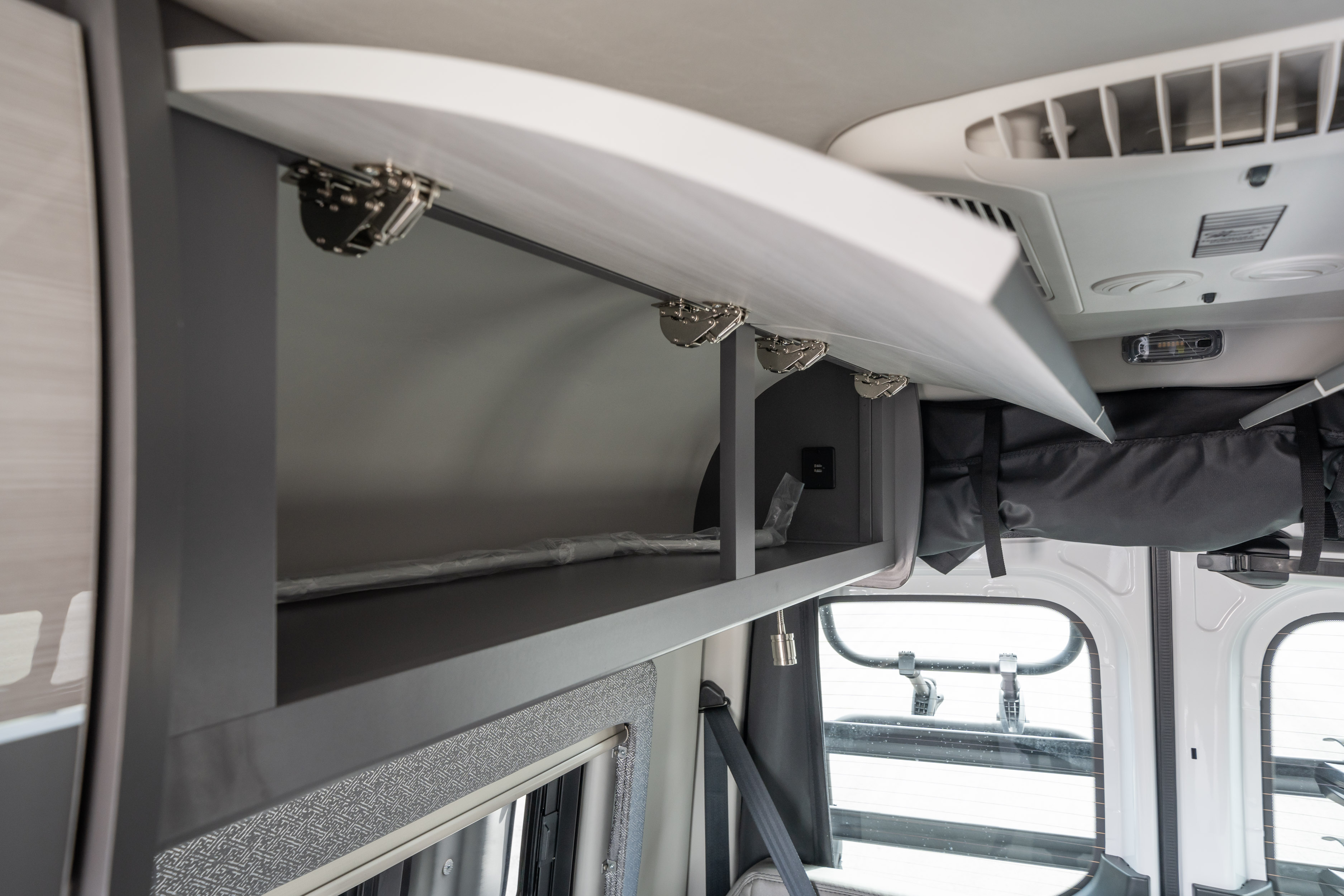 Inside an RV rental: open overhead cabinet with shelves and USB ports, ideal for travel storage and charging.. Thor Motor Coach Tranquility 4x4 2023
