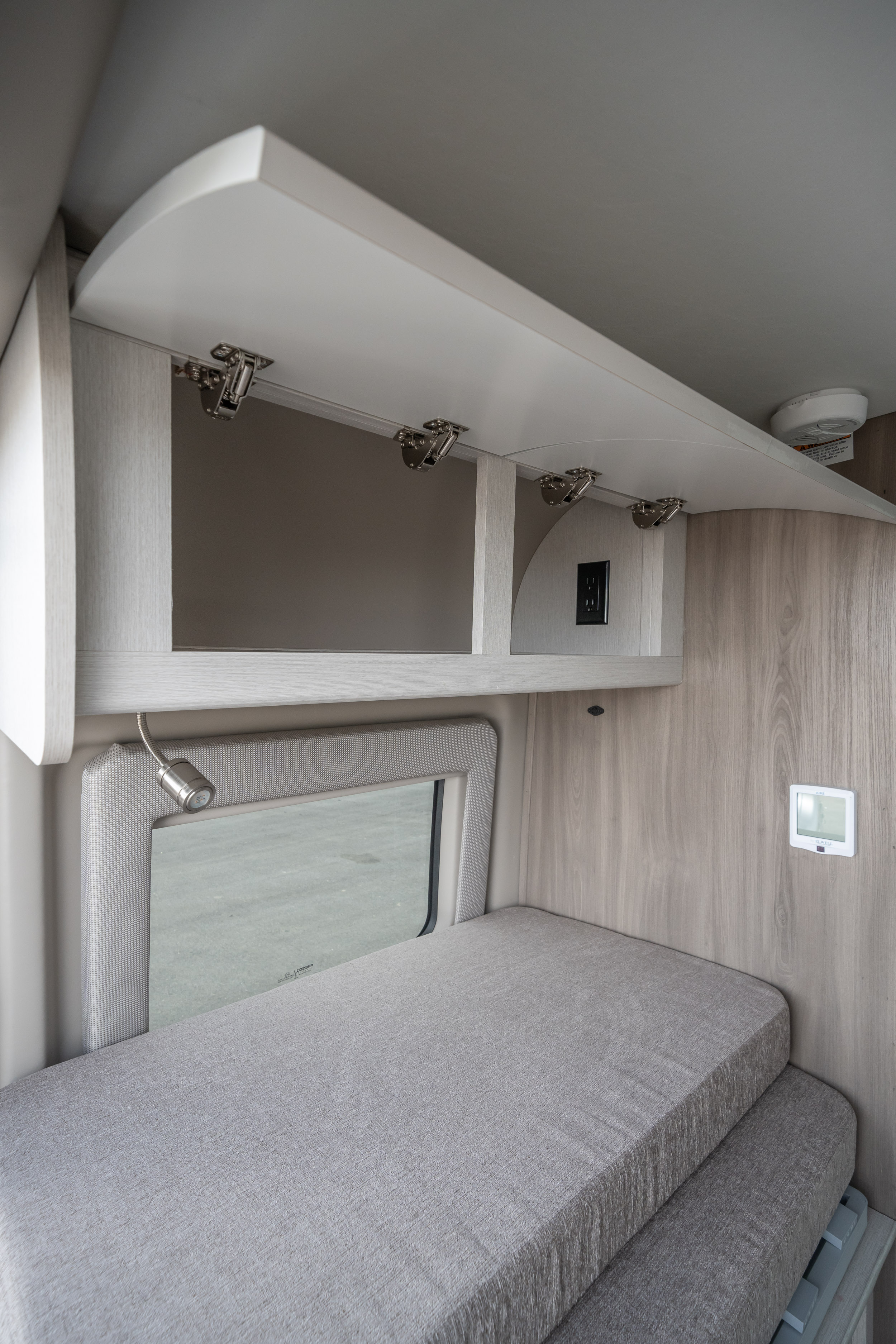 Detailed view of an RV rental's light-toned interior, featuring an open overhead cabinet, comfortable bed, and window. Ideal for compact living.. Thor Motor Coach Rize 2023