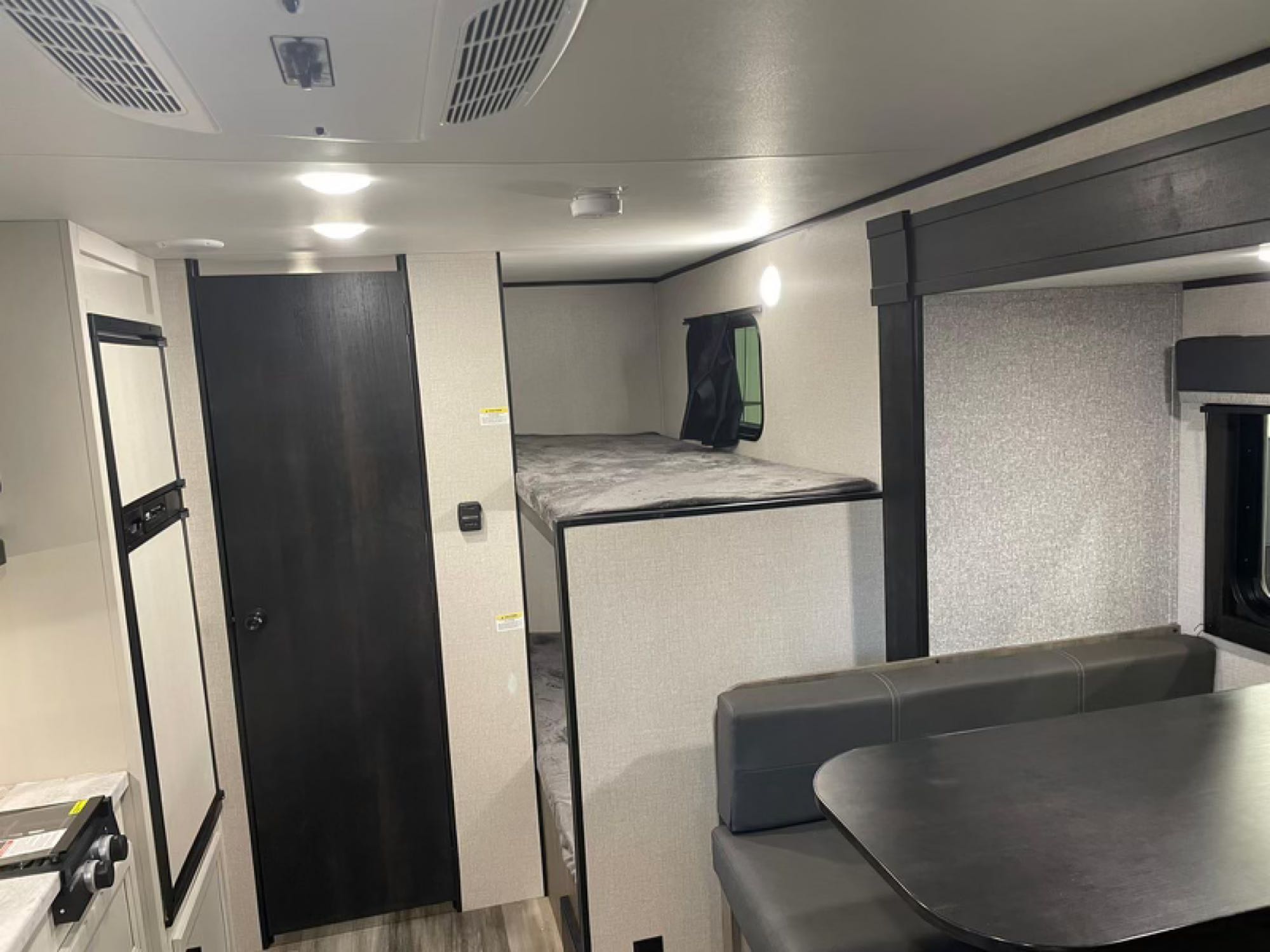 RV rental interior: view of a compact kitchen, dark door, bunk beds, and a grey dinette area with table.. Highland Ridge RV Open Range 2022