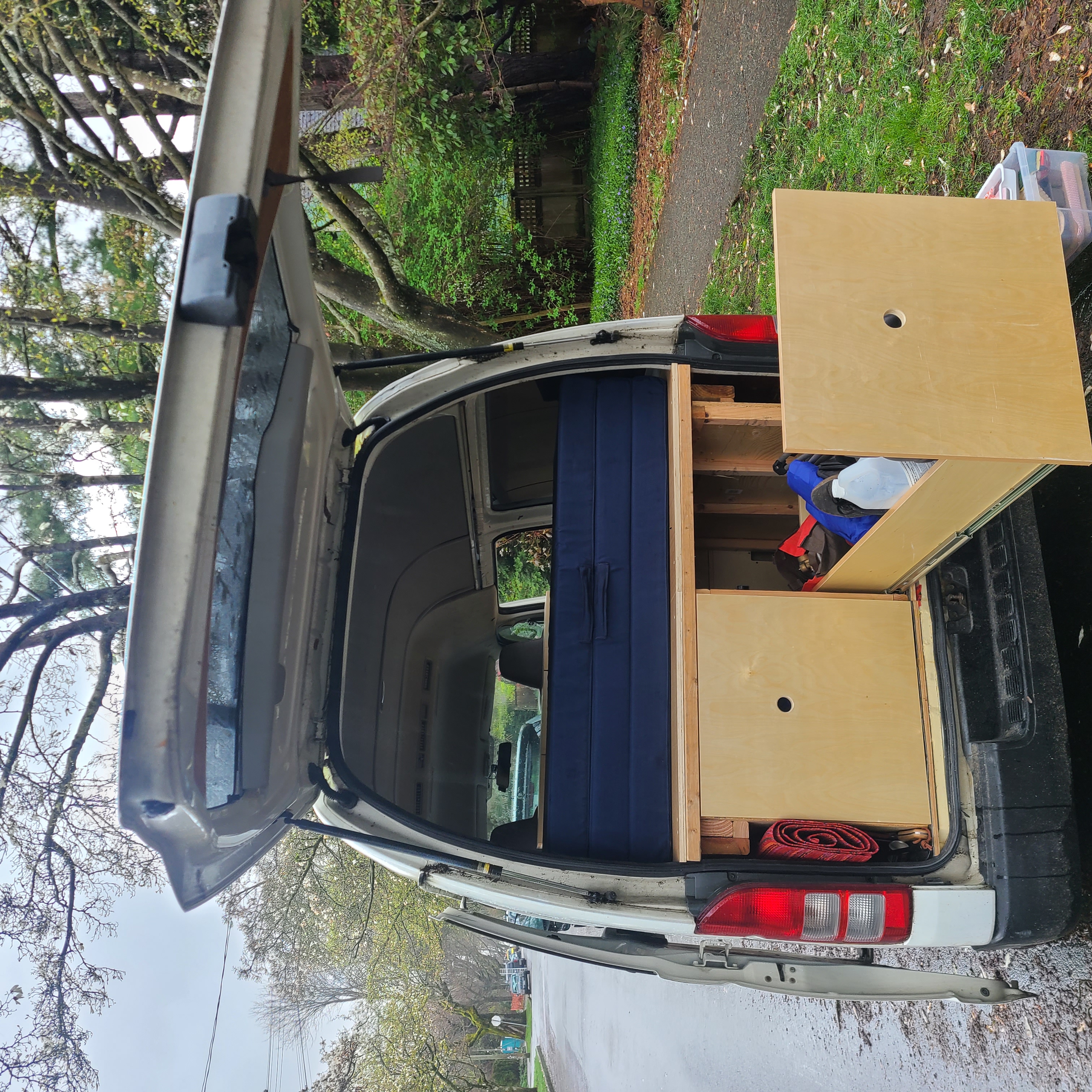 RV rental van's rear interior: custom bed and wooden storage setup, ideal for travel and mobile living.. Toyota Hiace 2006