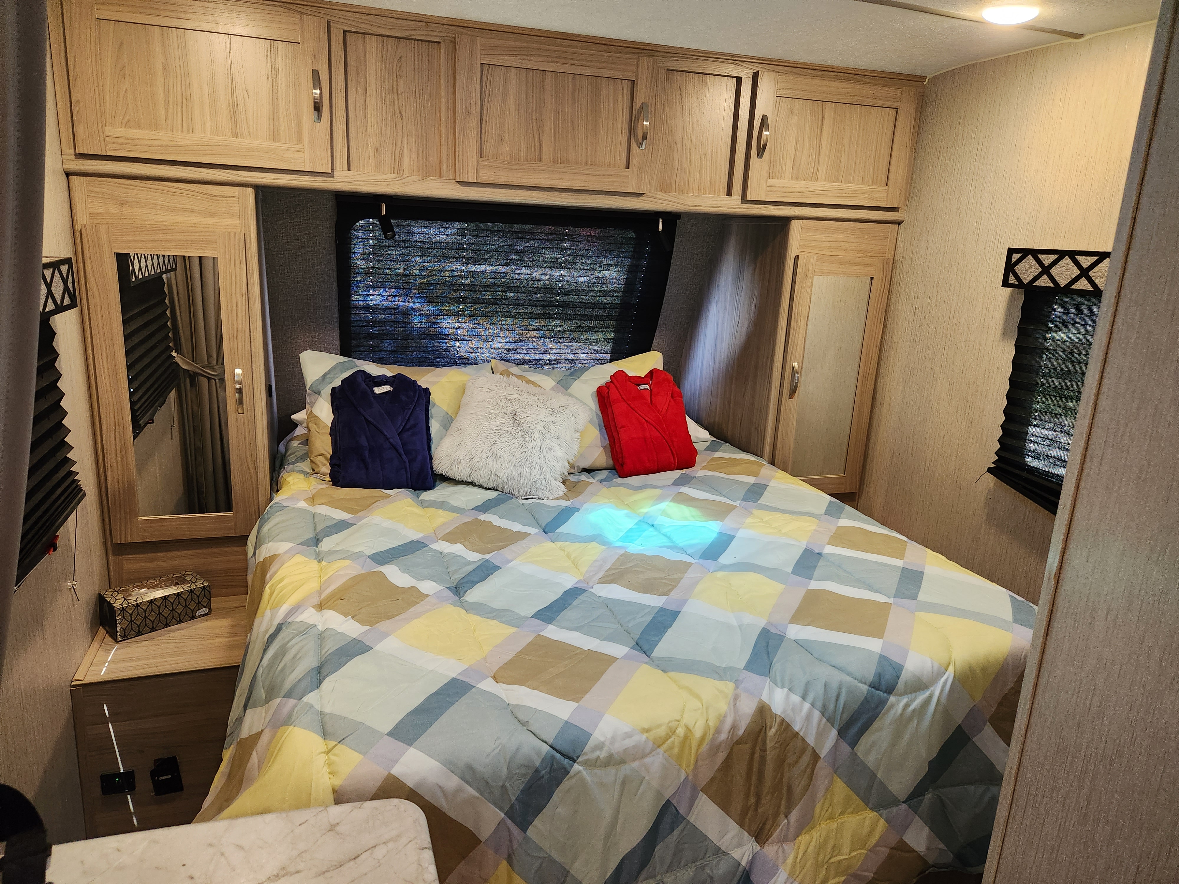 Cozy RV rental bedroom with a checkered bed, robes, and wooden storage cabinets, offering comfort on your adventures.. Coachmen Freedom Express 2021