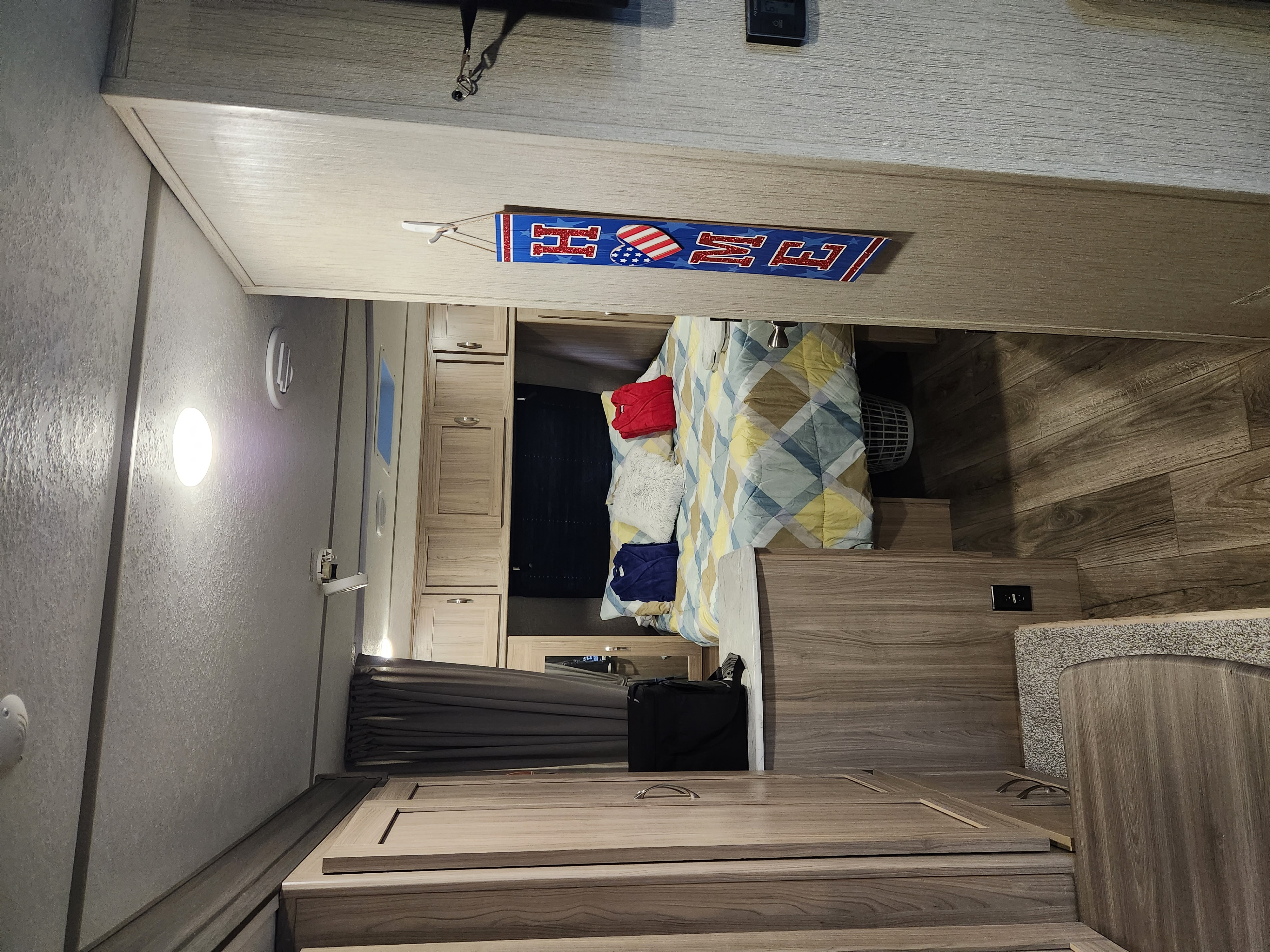 Interior of an RV rental: a comfortable and well-appointed bedroom with a patterned bed, wood cabinetry, and flooring.. Coachmen Freedom Express 2021