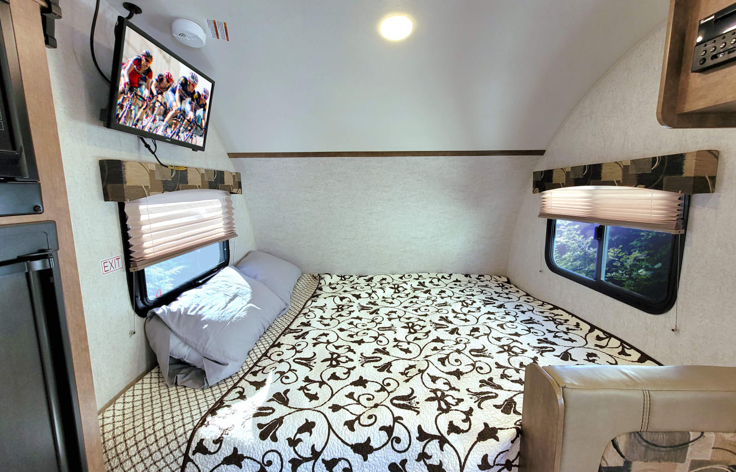 Compact RV rental bedroom with a comfy bed, TV showing cyclists, and scenic windows. A cozy sleeping area.. Starcraft Satellite 2018