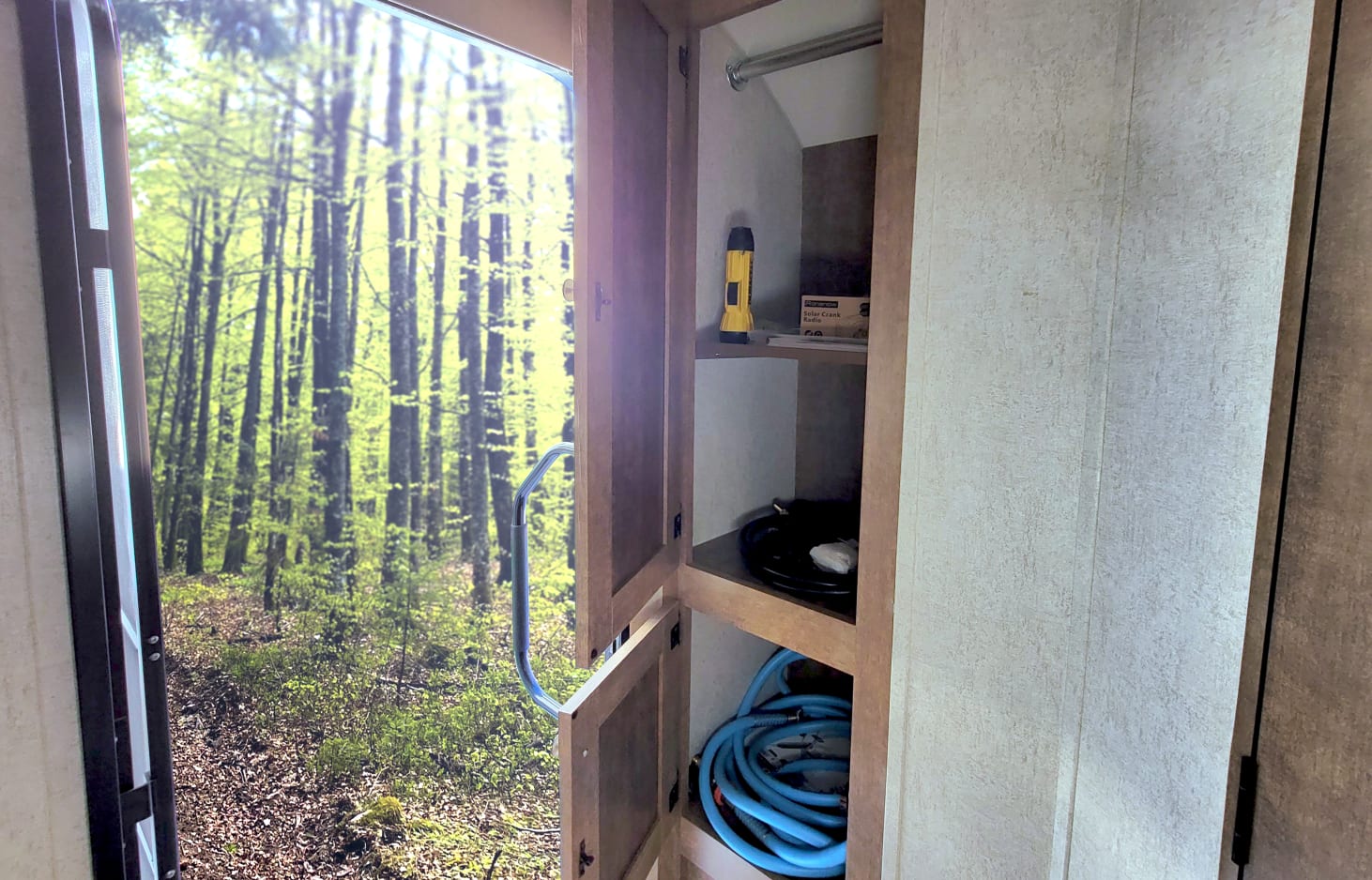 RV rental interior view: open door to a lush forest scene & organized cabinet with travel essentials like a solar radio & hoses.. Starcraft Satellite 2018