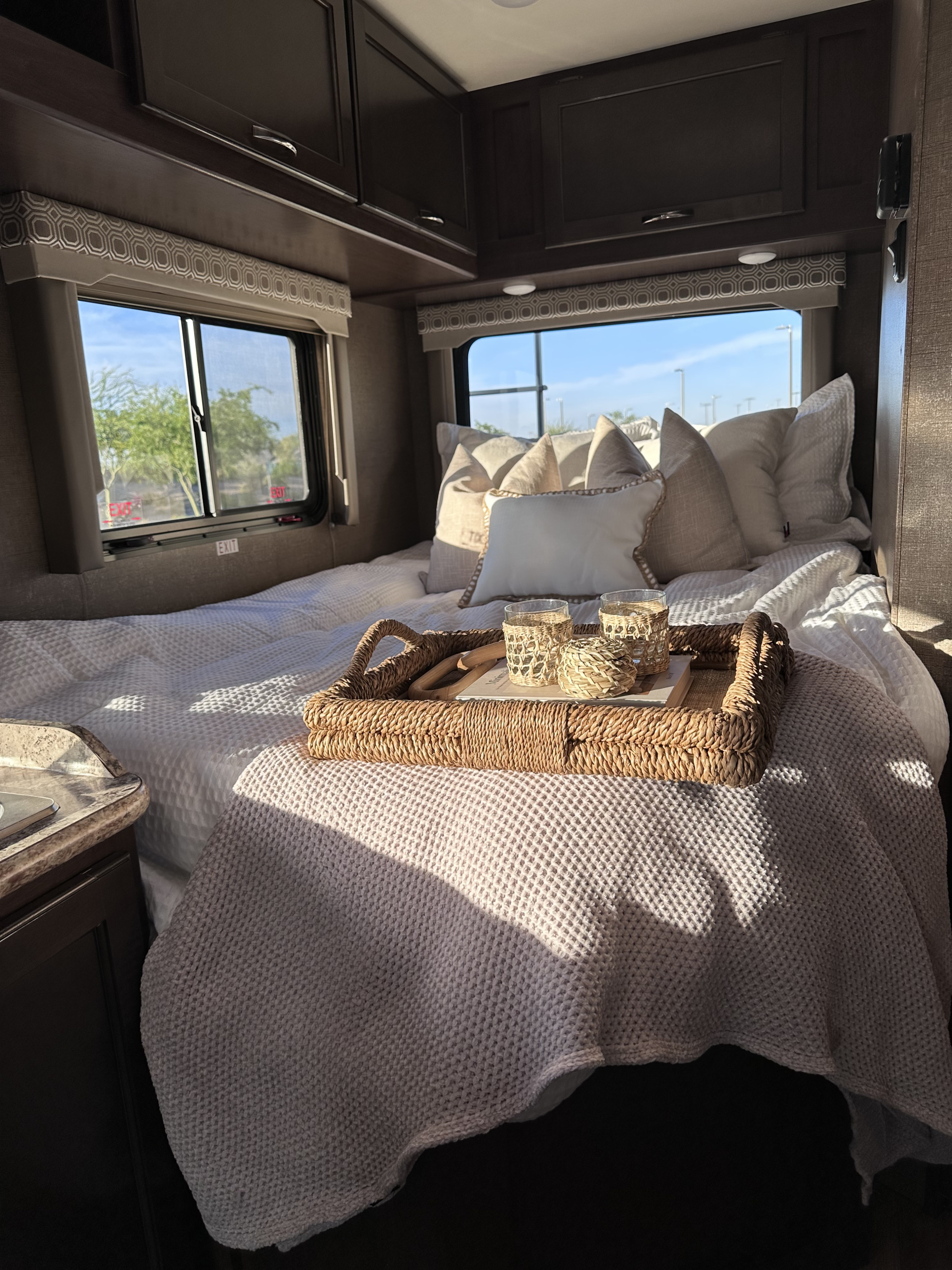 Sunny RV rental interior: A cozy bedroom space with a neatly made bed, decorative pillows, and a wicker tray with glasses.. Thor Four Winds 2020