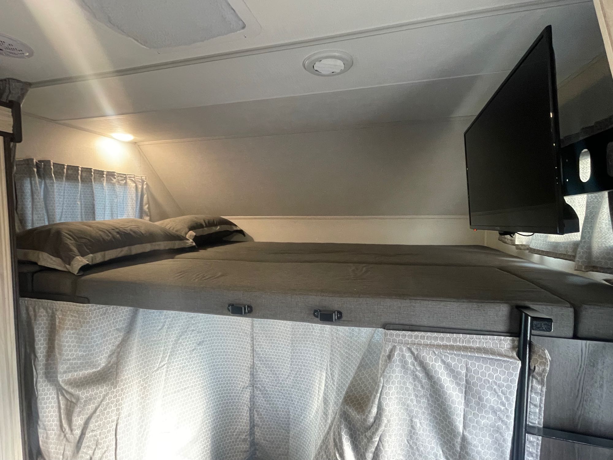 Inside an RV rental: elevated bunk bed with gray bedding, privacy curtains, and a mounted TV.. Forest River Forester 2022