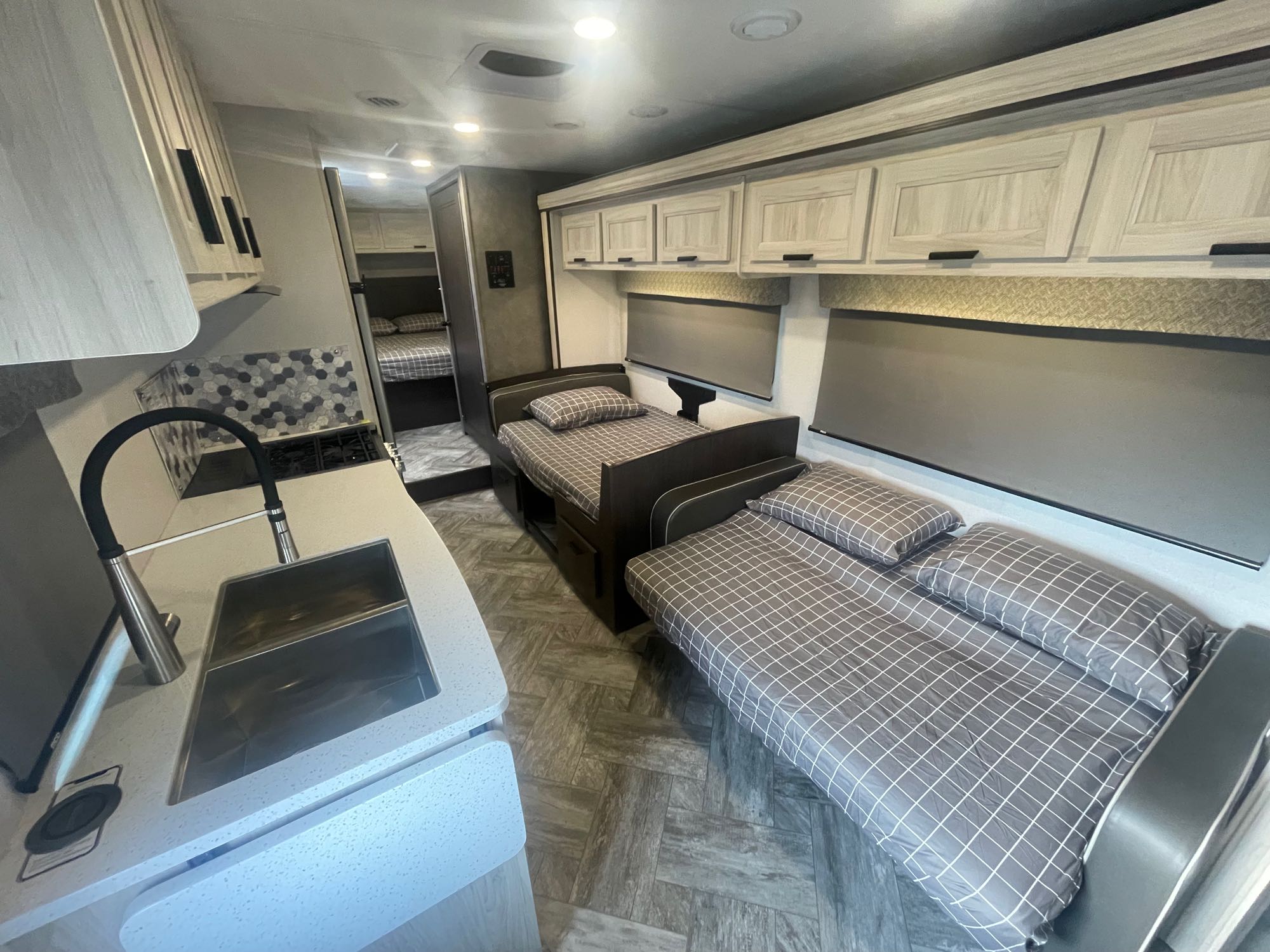 Inside a modern **RV rental** featuring a compact kitchen with sink, multiple neatly arranged beds, and overhead cabinets for storage.. Forest River Forester 2022