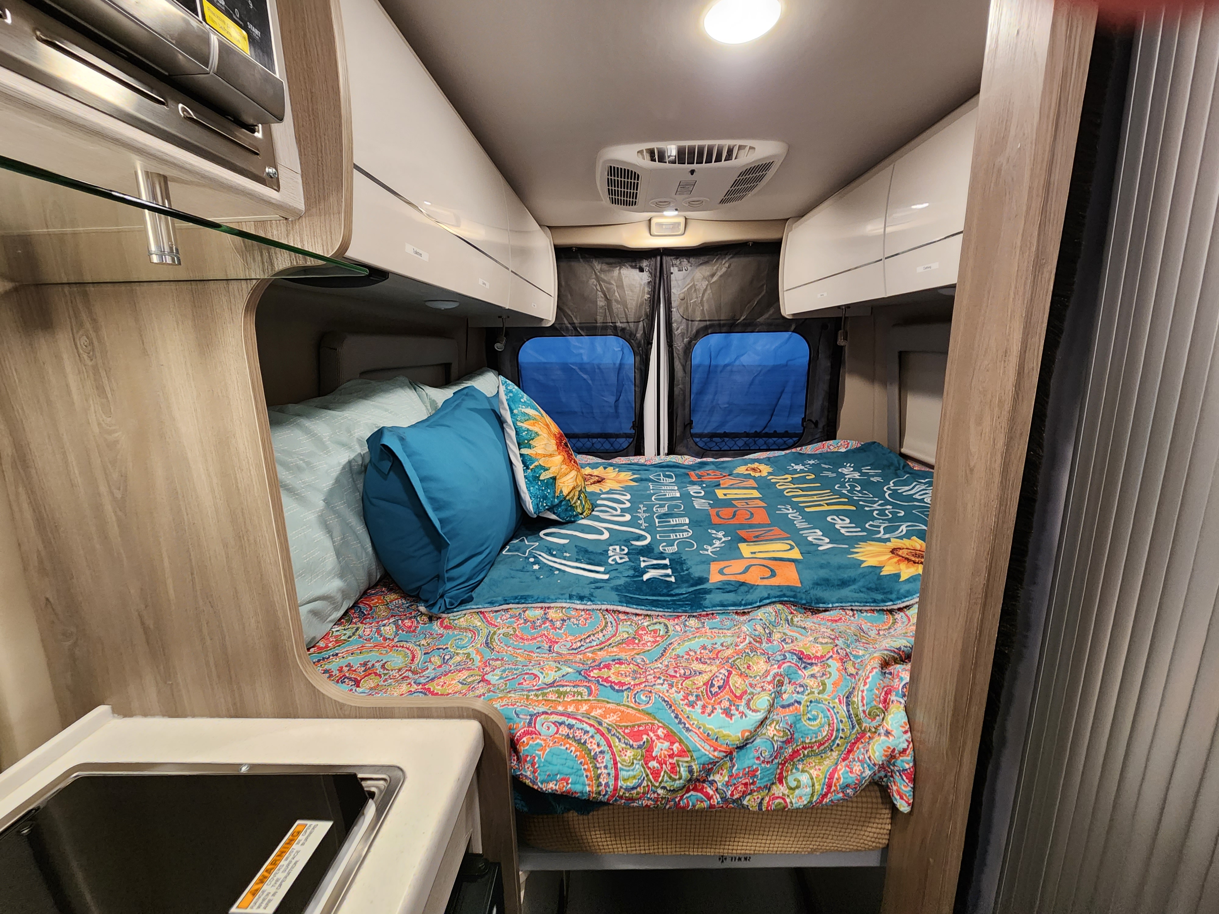Step inside this RV rental: a snug camper van with a vibrant bed, overhead storage, and compact kitchen area for travel.. Thor Tellaro 2023