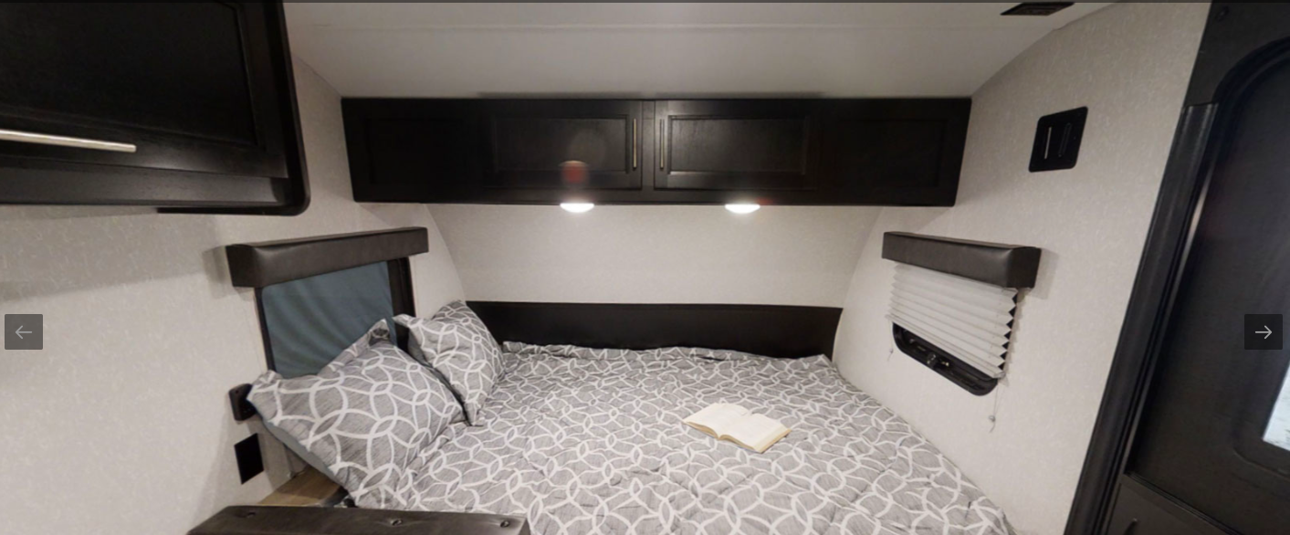 Compact RV rental sleeping area featuring a patterned bed, storage cabinets, and window blinds.. Forest River Cherokee Wolf Pup 2022