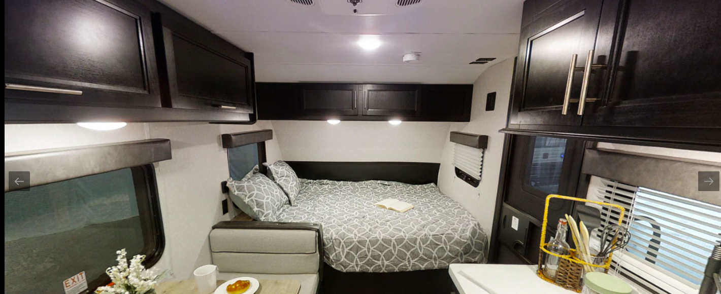 Inside an RV rental: a compact living area featuring a comfortable bed, overhead cabinets, and a small dinette with kitchen space.. Forest River Cherokee Wolf Pup 2022