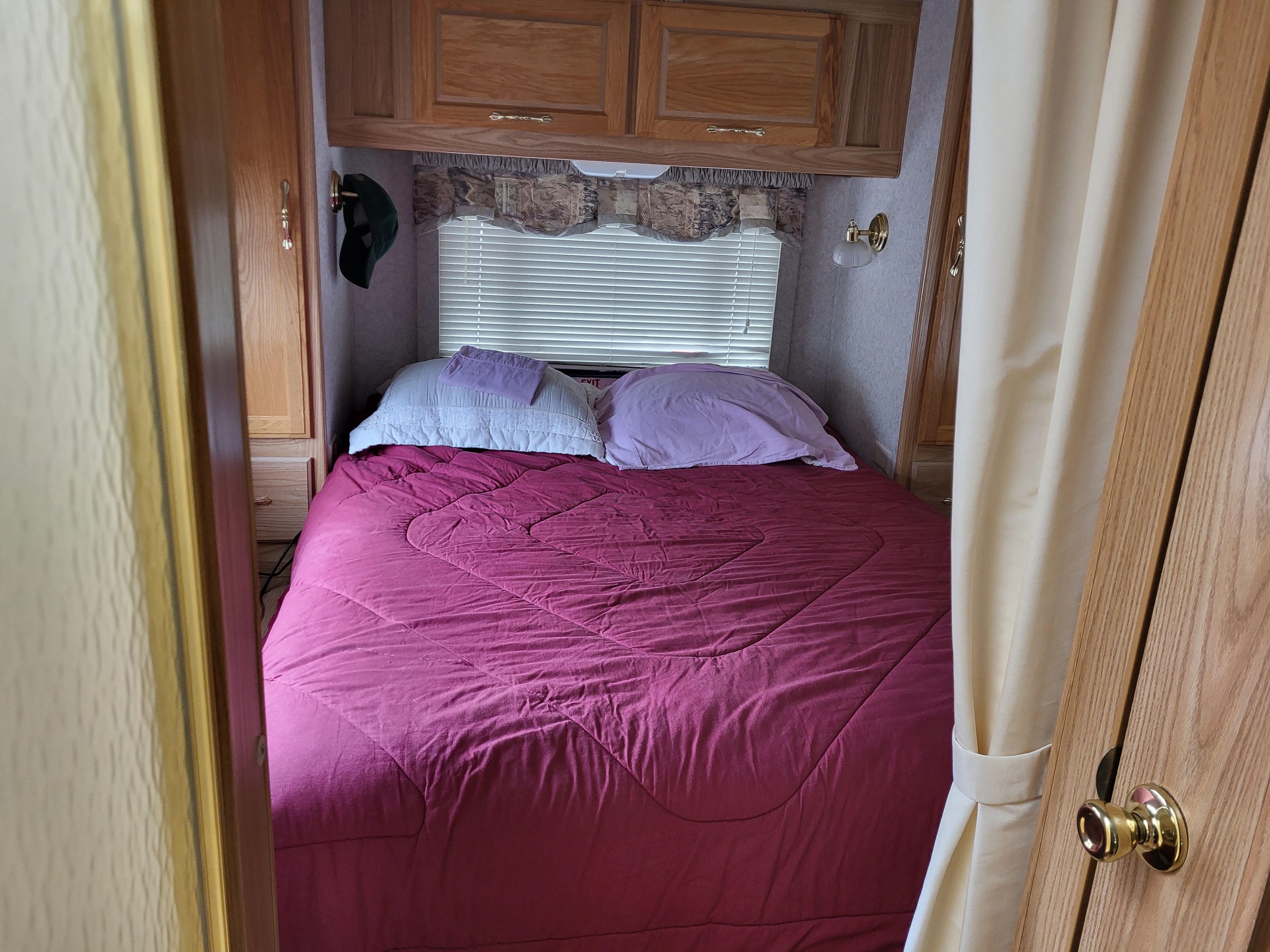 Inviting RV rental bedroom: cozy bed with maroon comforter, pillows, window with blinds, and wood storage cabinets.. Tioga Tioga Motorhome 2001