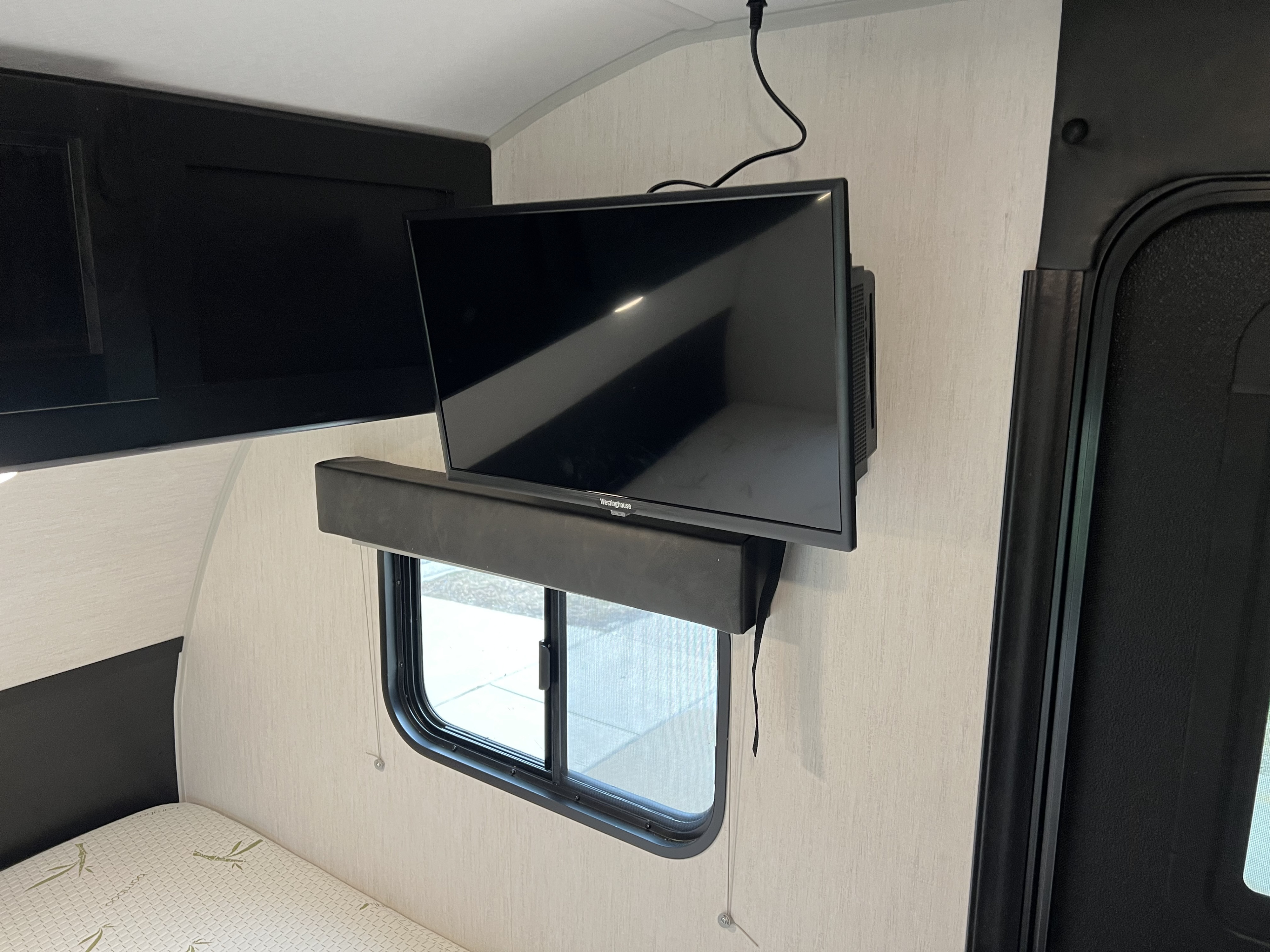 RV rental interior: wall-mounted TV, window with blind, and bed area. Cozy camper amenities for travel.. Forest River 16ts 2022