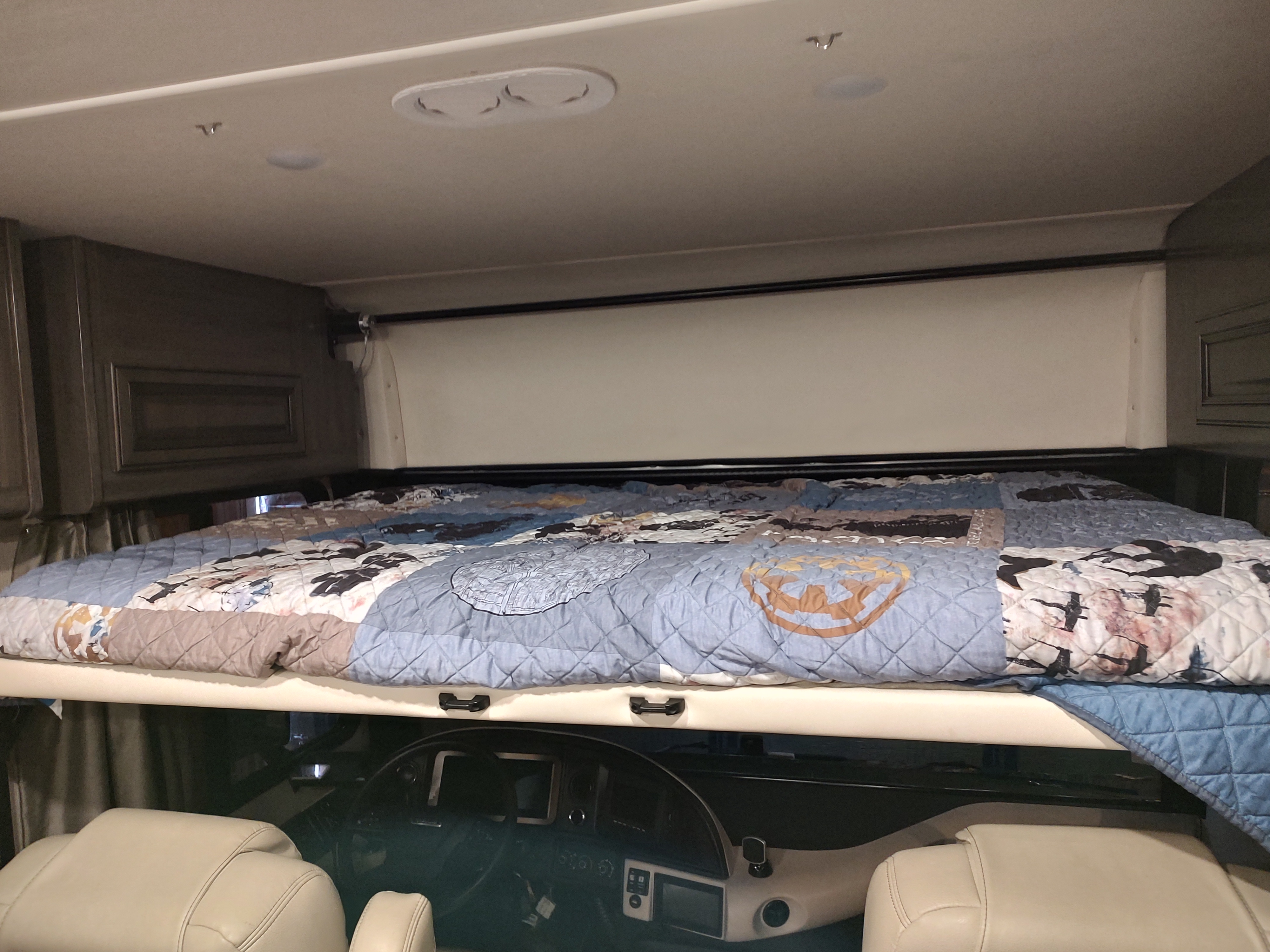 **RV rental** sleeping area: A cozy, patterned bed is positioned over the driver's cabin in a motorhome.. Fleetwood Pace Arrow 35QS 2021