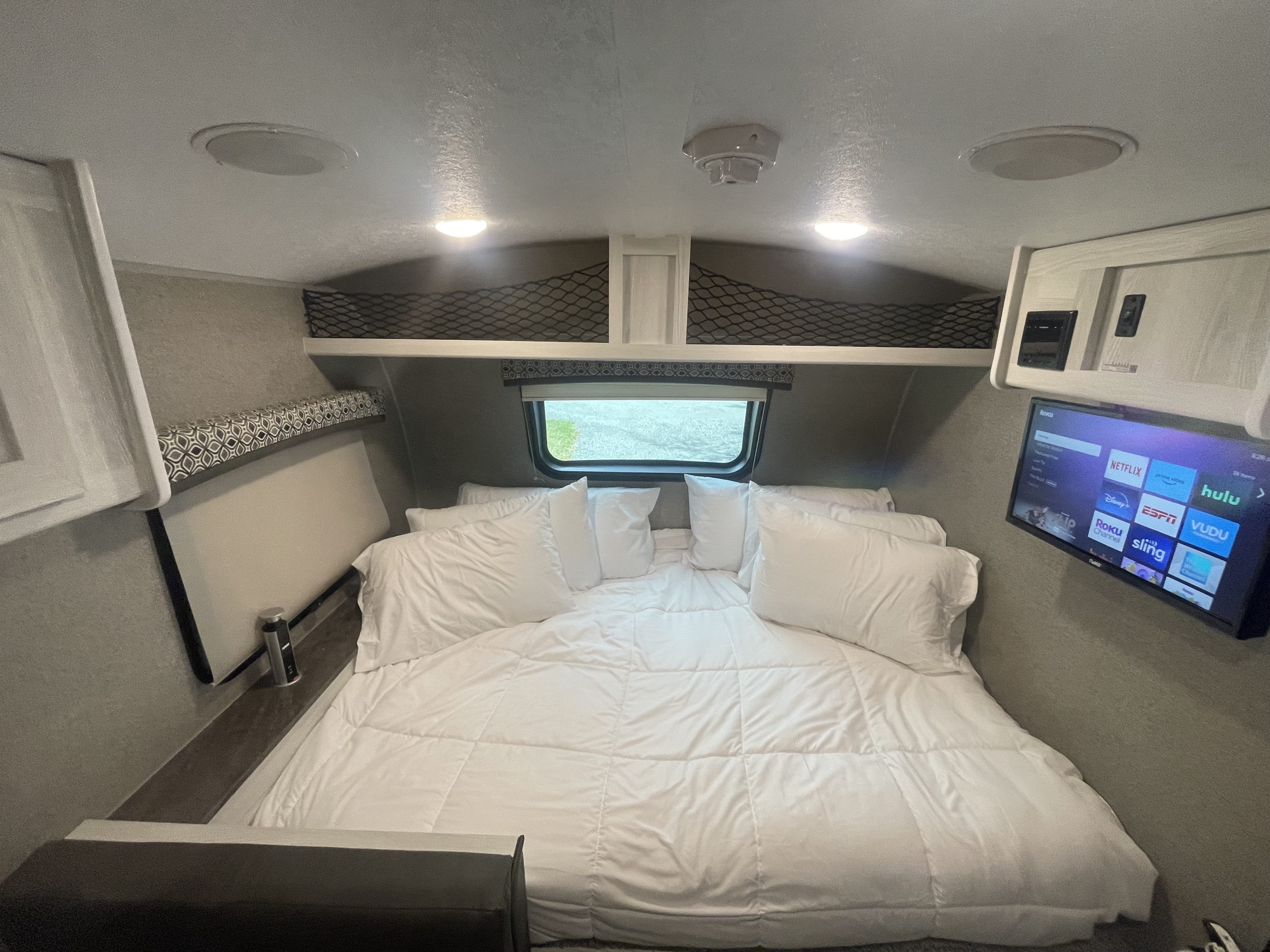 Cozy RV rental bedroom featuring a large bed with white linens, smart TV, overhead storage nets, and ambient lighting.. Forest River Flagstaff E-Pro 2020