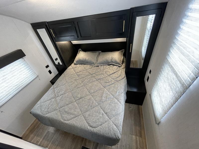 Cozy RV rental bedroom with a grey bed, dark overhead cabinets, and mirrored storage on both sides. Windows offer natural light.. Forest River Cherokee 2022