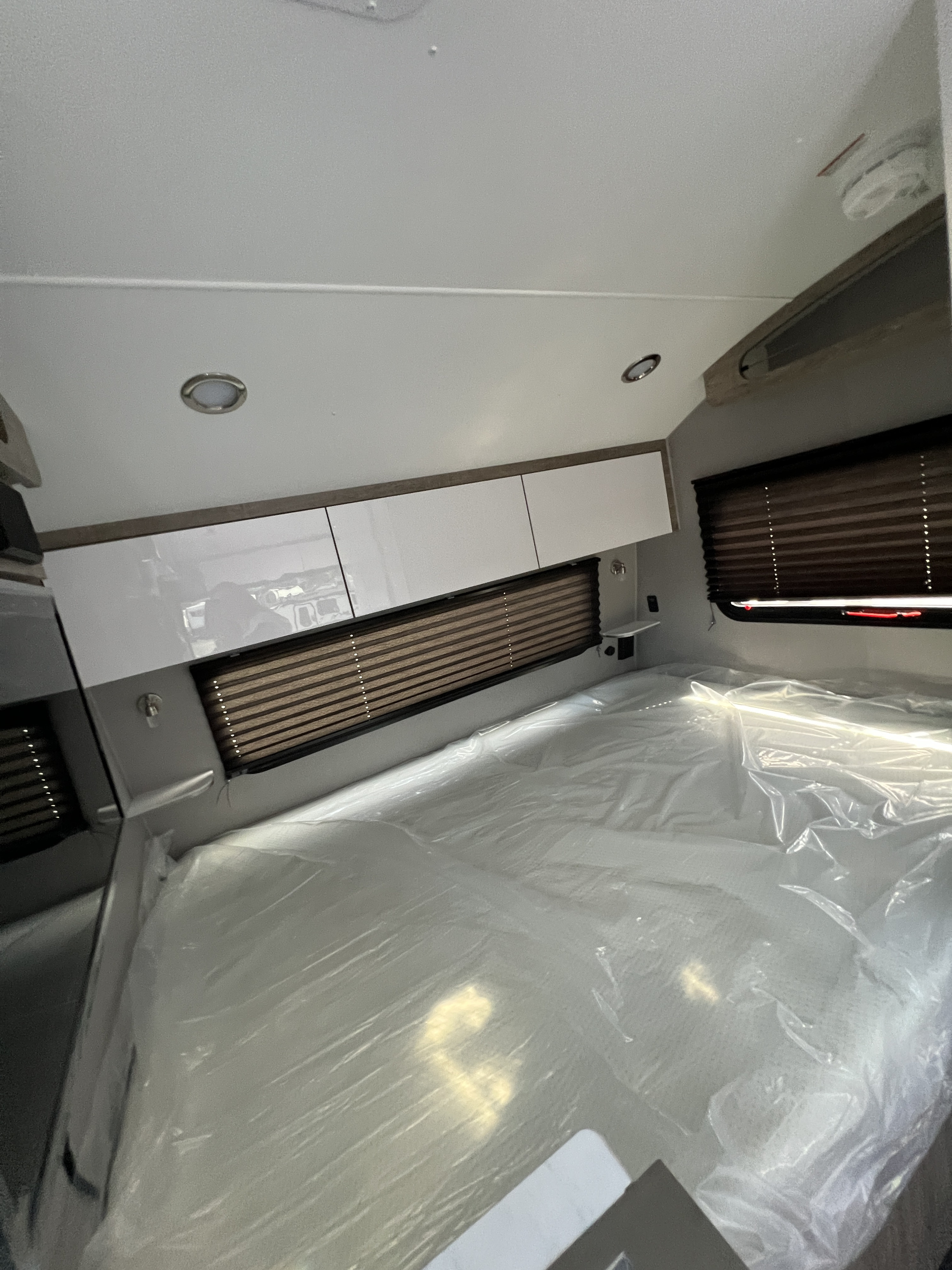 Bright RV rental bedroom showing a new, plastic-wrapped mattress, sleek overhead cabinets, and window blinds.. Travel Lite Other 2023