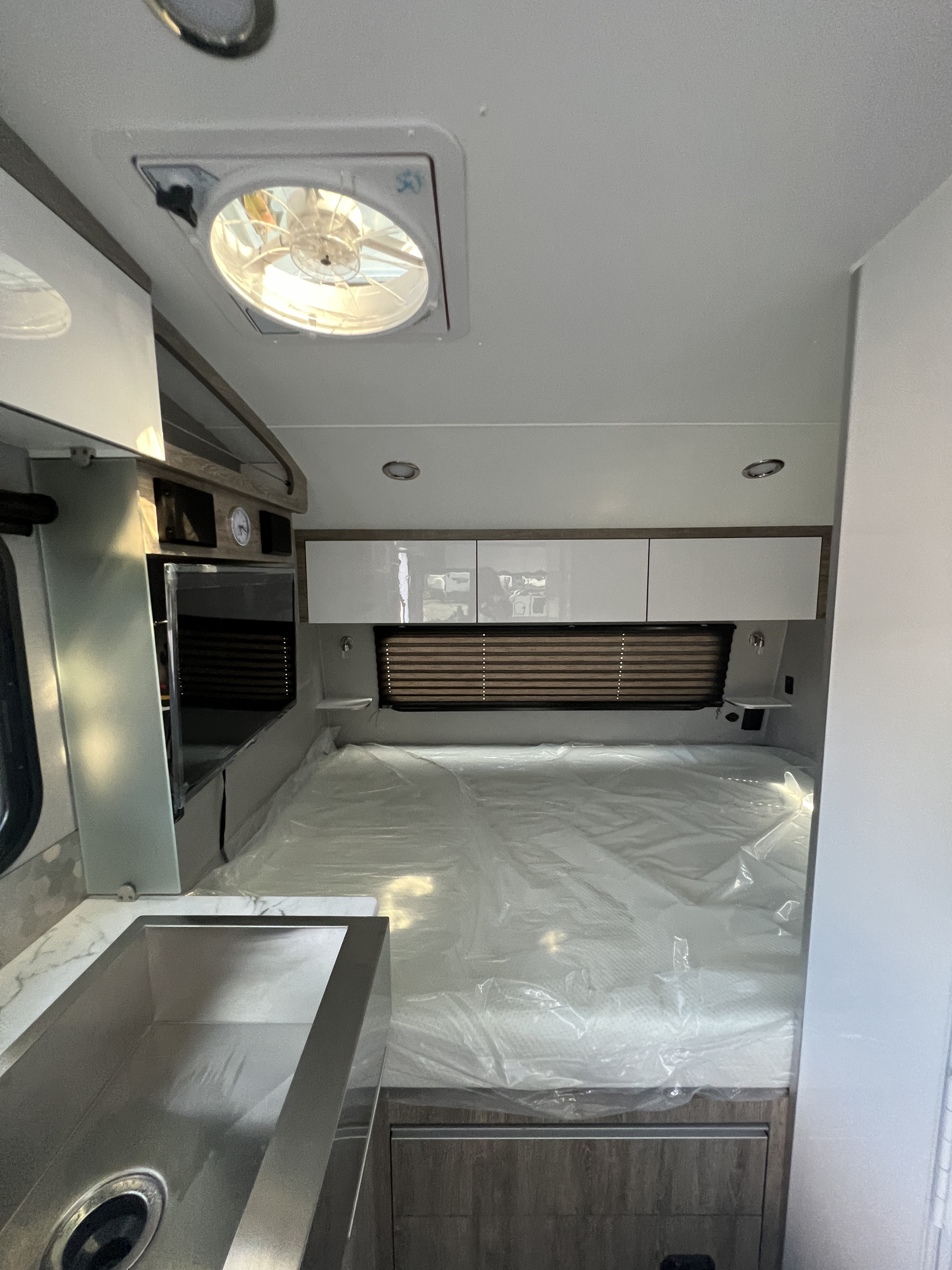 Inside a clean RV rental: A compact bedroom with new mattress, kitchen sink area, and ample storage for travel.. Travel Lite Other 2023