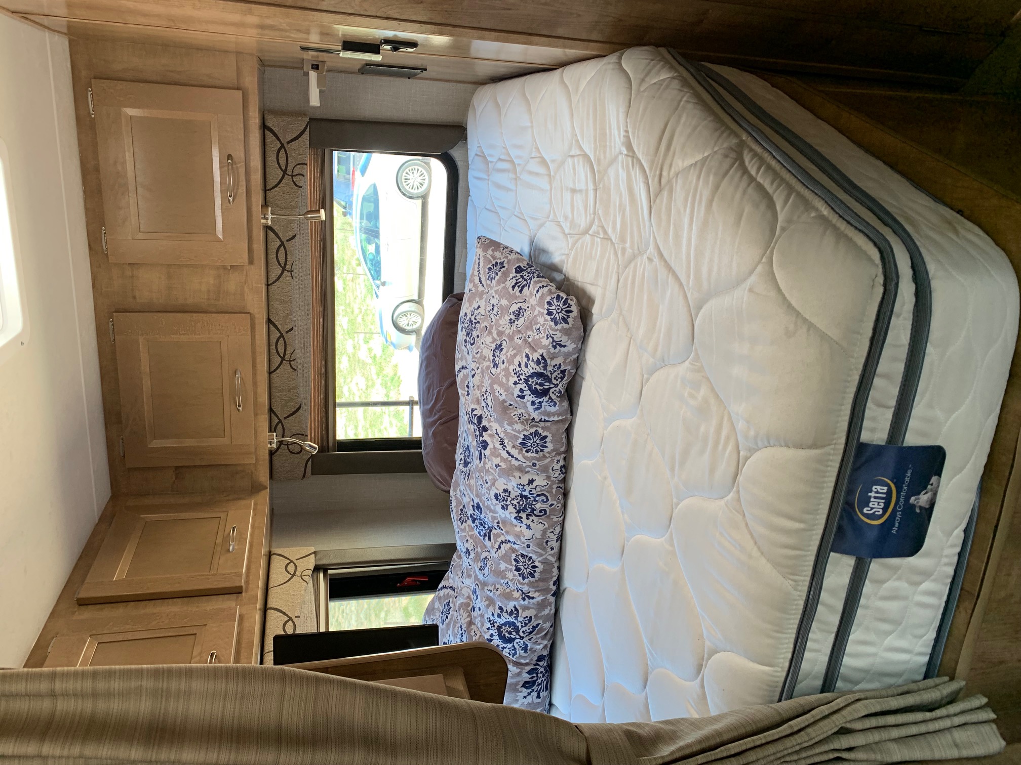 Cozy RV rental bedroom featuring a comfortable Serta mattress, patterned pillow, and practical wooden cabinets.. FORD E350 2020