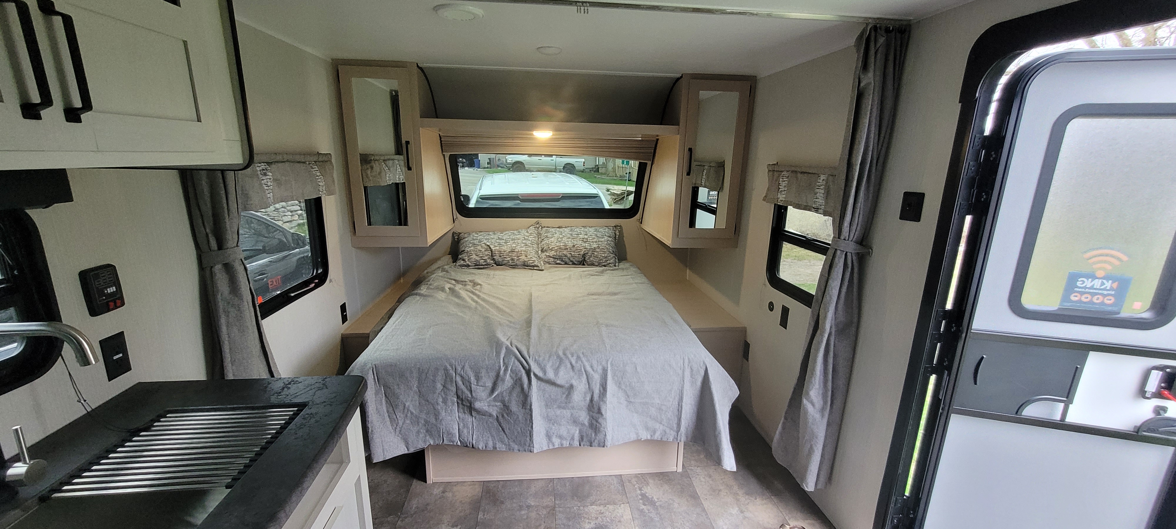 Interior of an rv rental, showing a bedroom area with a bed, overhead storage, windows, and a sink to the left. Compact and functional.. Forest River Palomino Puma 2023