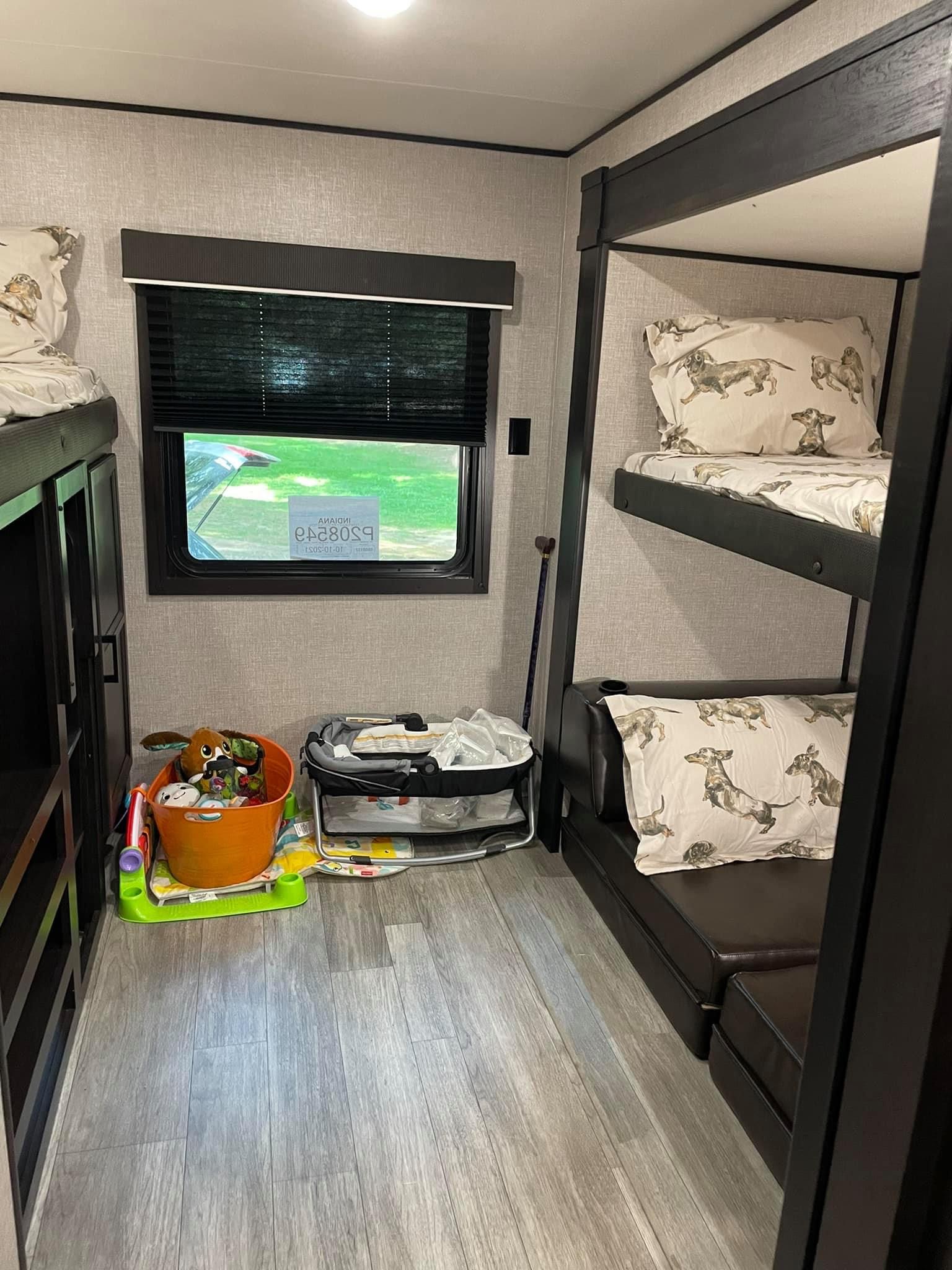 An RV rental interior with black bunk beds, playful dachshund pillows, and child's toys by a window.. Jayco Jay Flight 2022