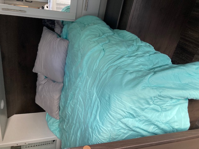 Cozy bed inside an RV rental, featuring a vibrant aqua comforter and soft gray pillows, ready for a restful sleep.. Keystone RV Bullet Ultra Lite 2021