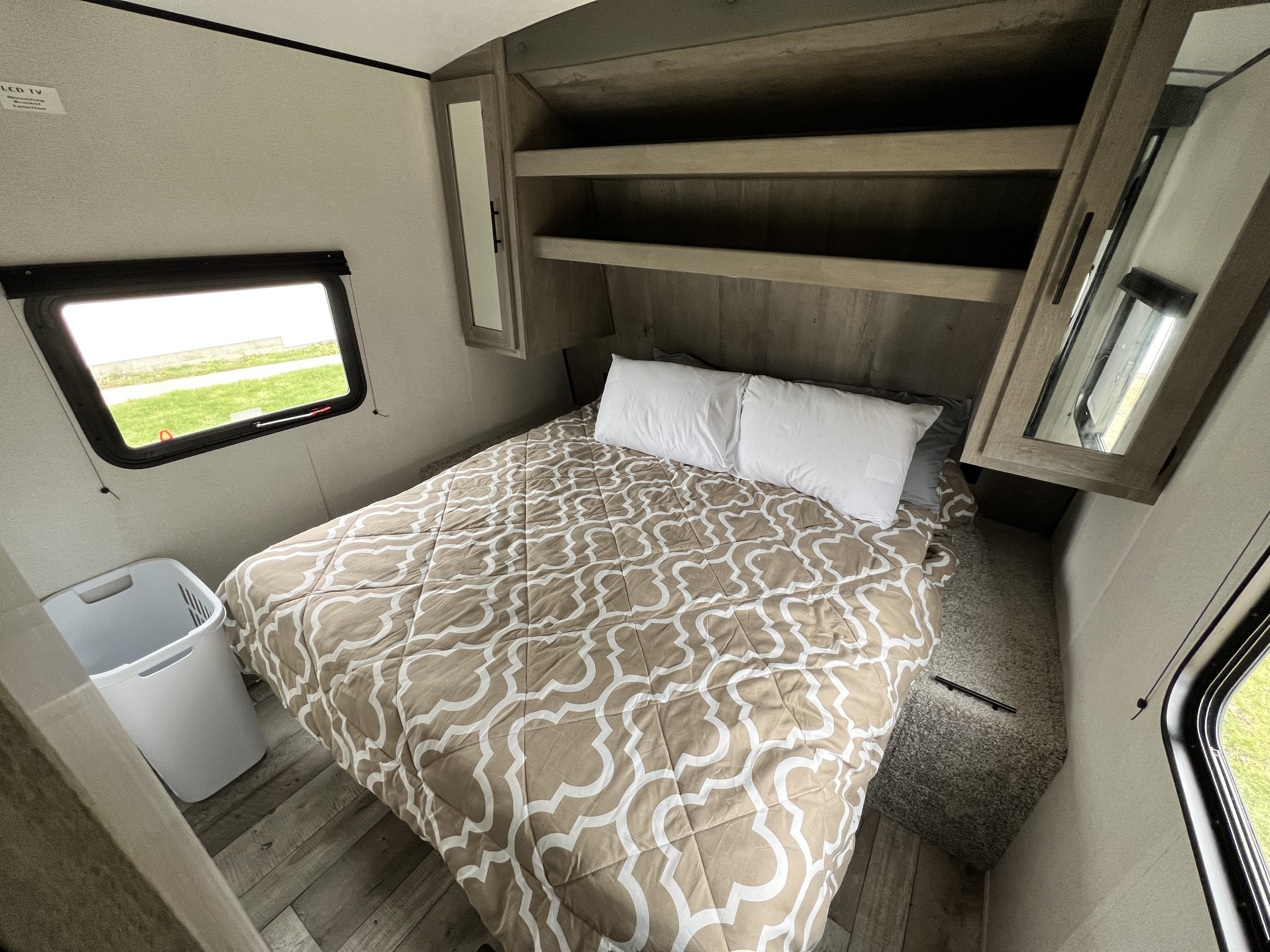 This RV rental bedroom offers a comfortable bed, overhead storage, mirrored cabinets, and a window with an outdoor view.. Keystone Springdale 2021