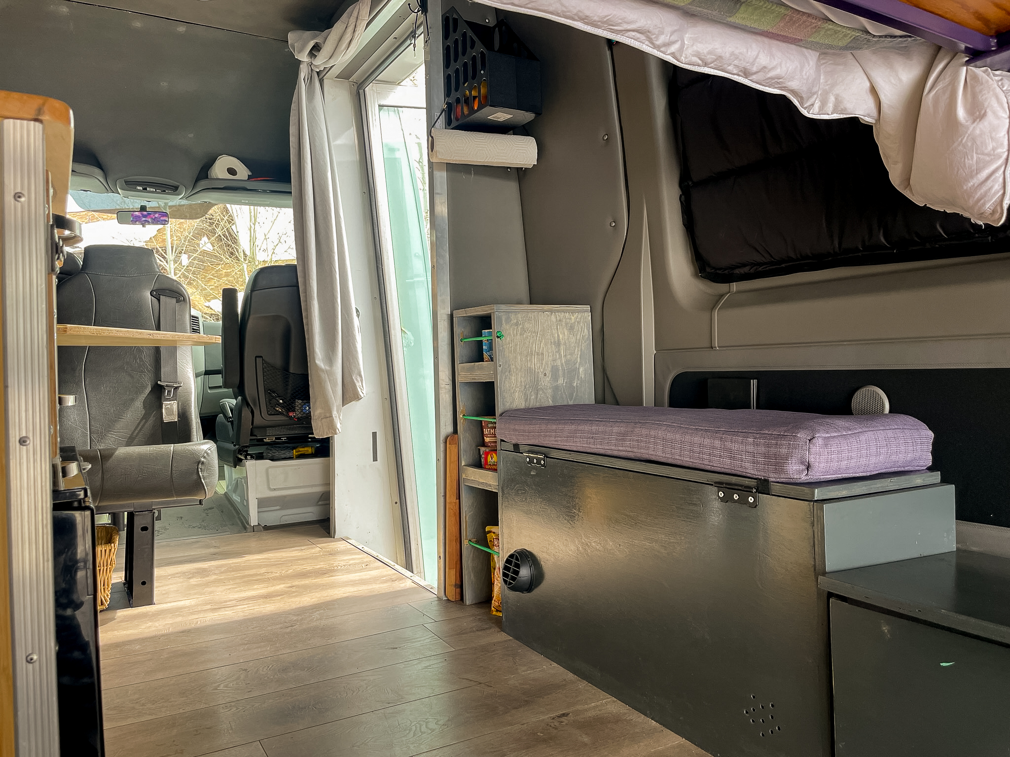 Inside this custom RV rental: wood floor, front seats, kitchen shelf, and a purple-cushioned bench. Ideal mobile living.. Mercedes-Benz Sprinter 2012