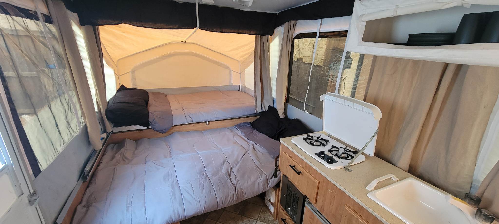 RV rental interior: Cozy pop-up camper with two beds, a small kitchenette (stove, sink), and windows, ready for camping.. Forest River Flagstaff 2008