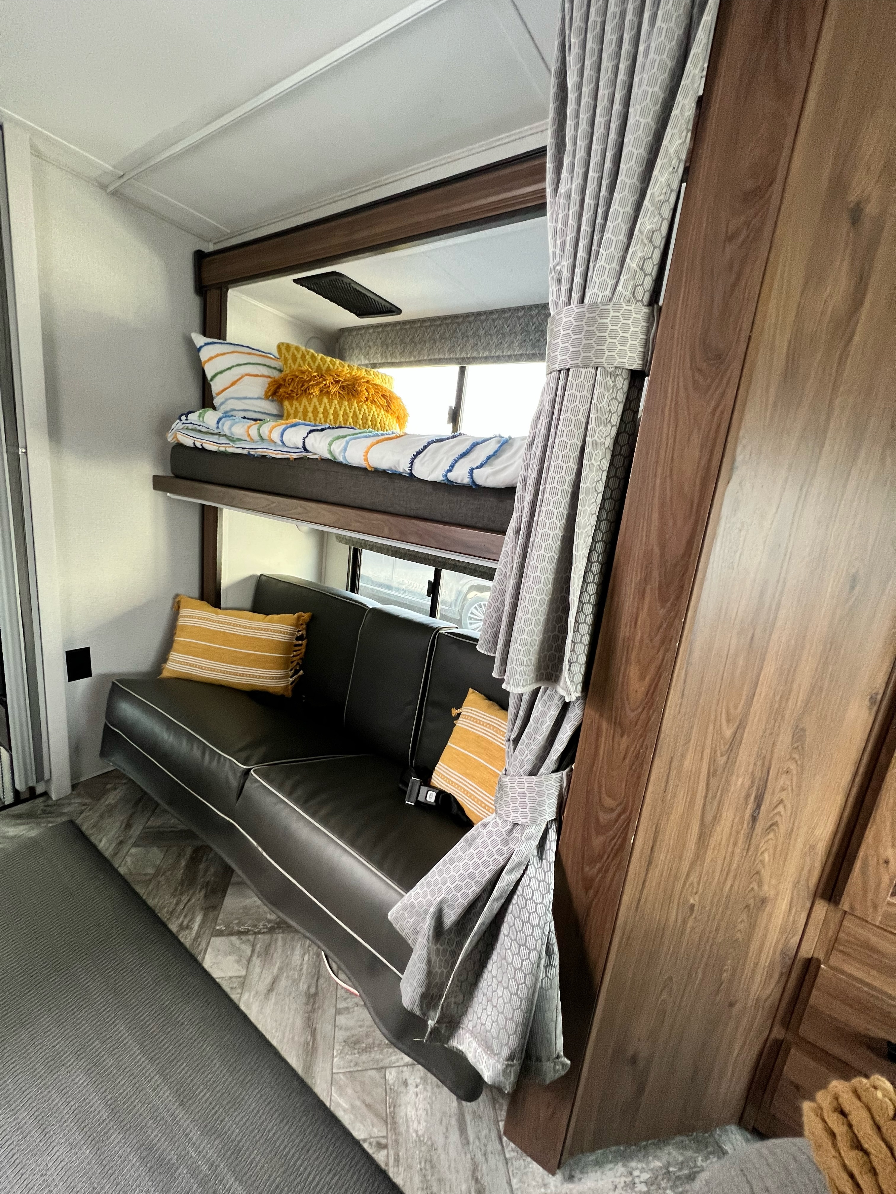 Cozy RV rental interior featuring a bunk bed with colorful bedding above a comfortable black couch, perfect for compact living.. Forest River Forester 2022