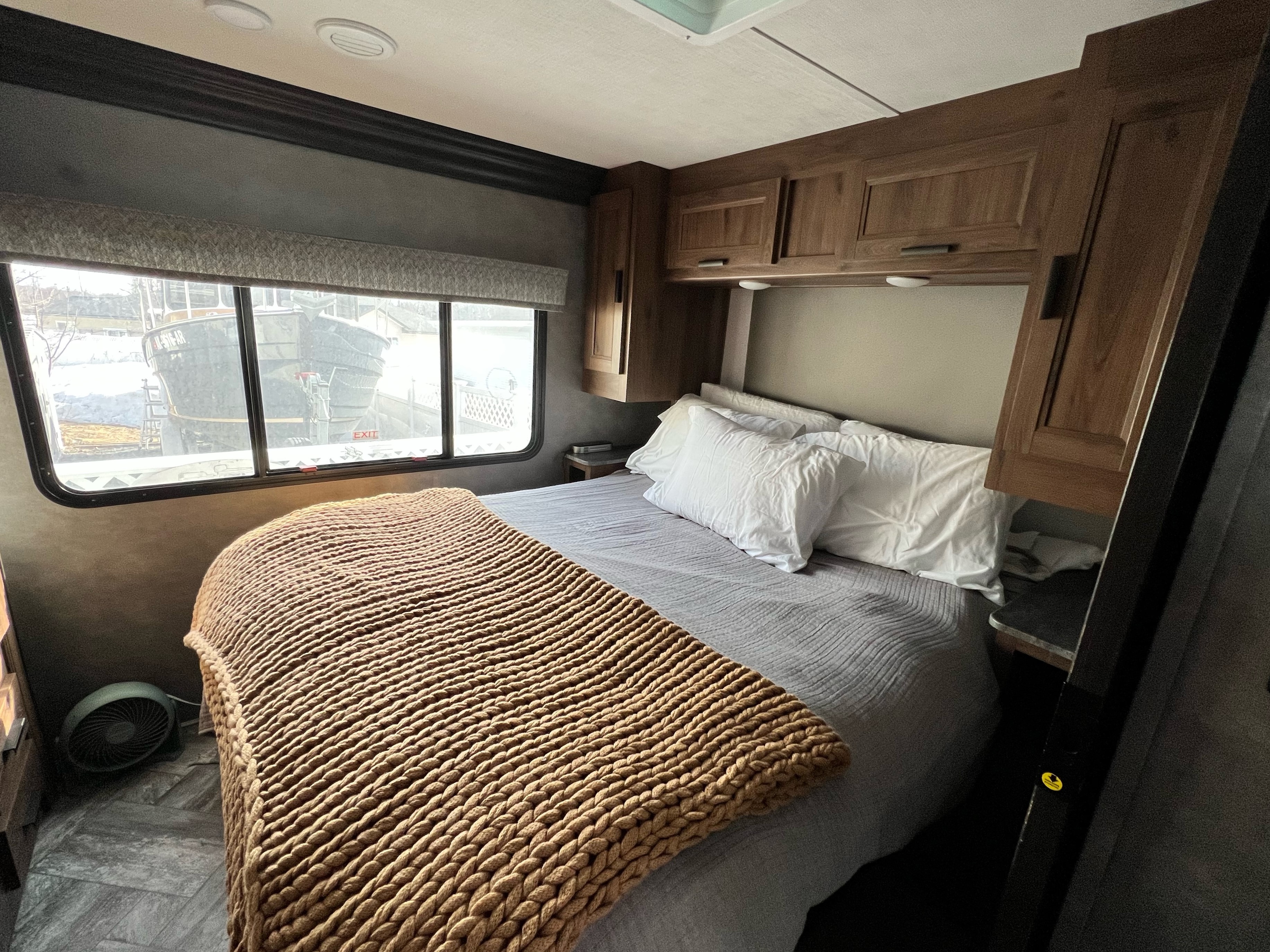 Cozy RV rental bedroom with a large bed, warm blanket, wooden cabinets, and a window showing a boat in snowy conditions outside.. Forest River Forester 2022
