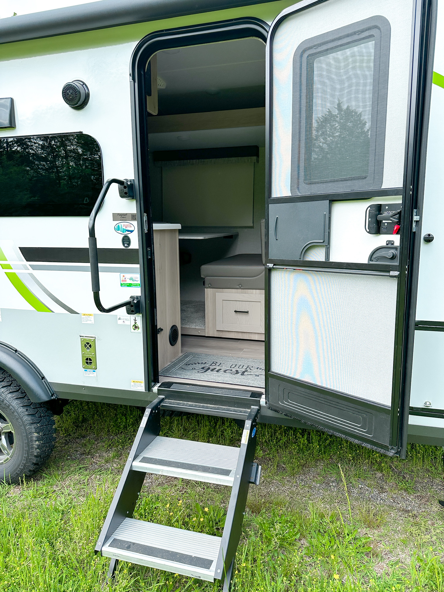 An open RV rental entrance, showcasing aluminum steps, screen door, and a welcoming interior of a travel trailer.. Forest River Flagstaff E-Pro 2023