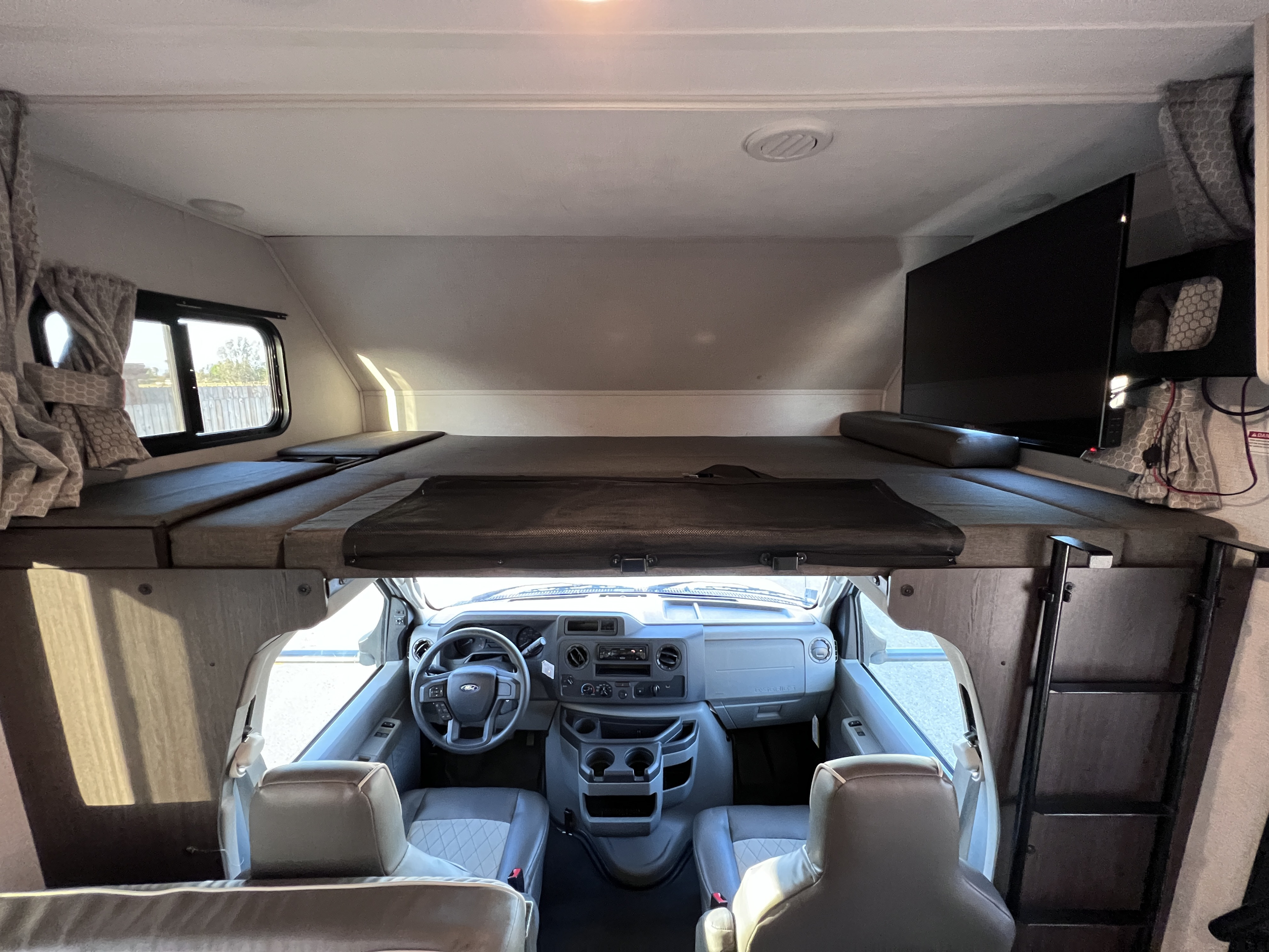 Inside a modern rv rental: a spacious cab-over bunk, TV, and cockpit. Ladder to bed, ready for travel!. Forest River Sunseeker LE 2022