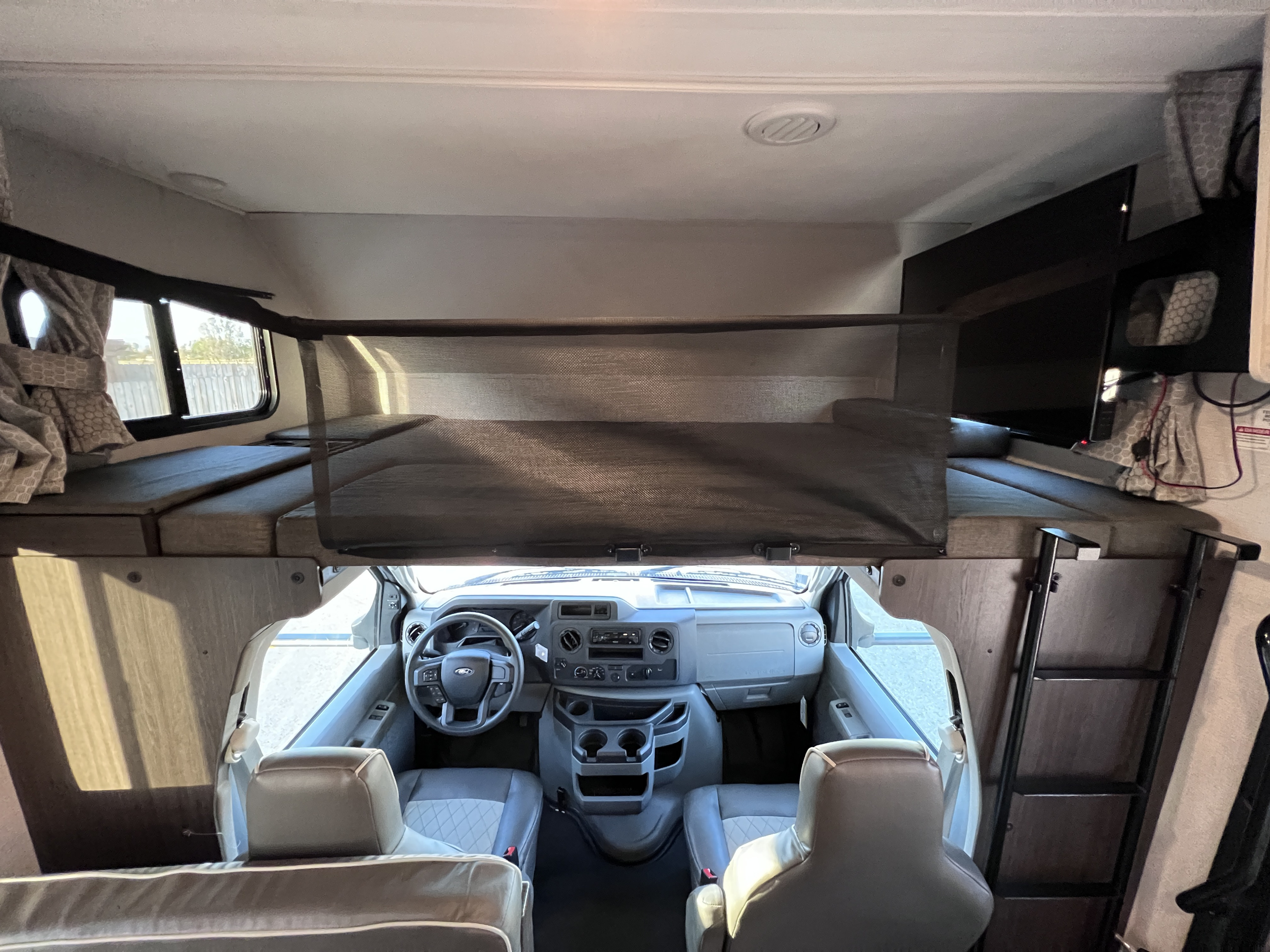 View inside an RV rental, showing the over-cab bunk bed with safety net, and driver's cockpit below.. Forest River Sunseeker LE 2022