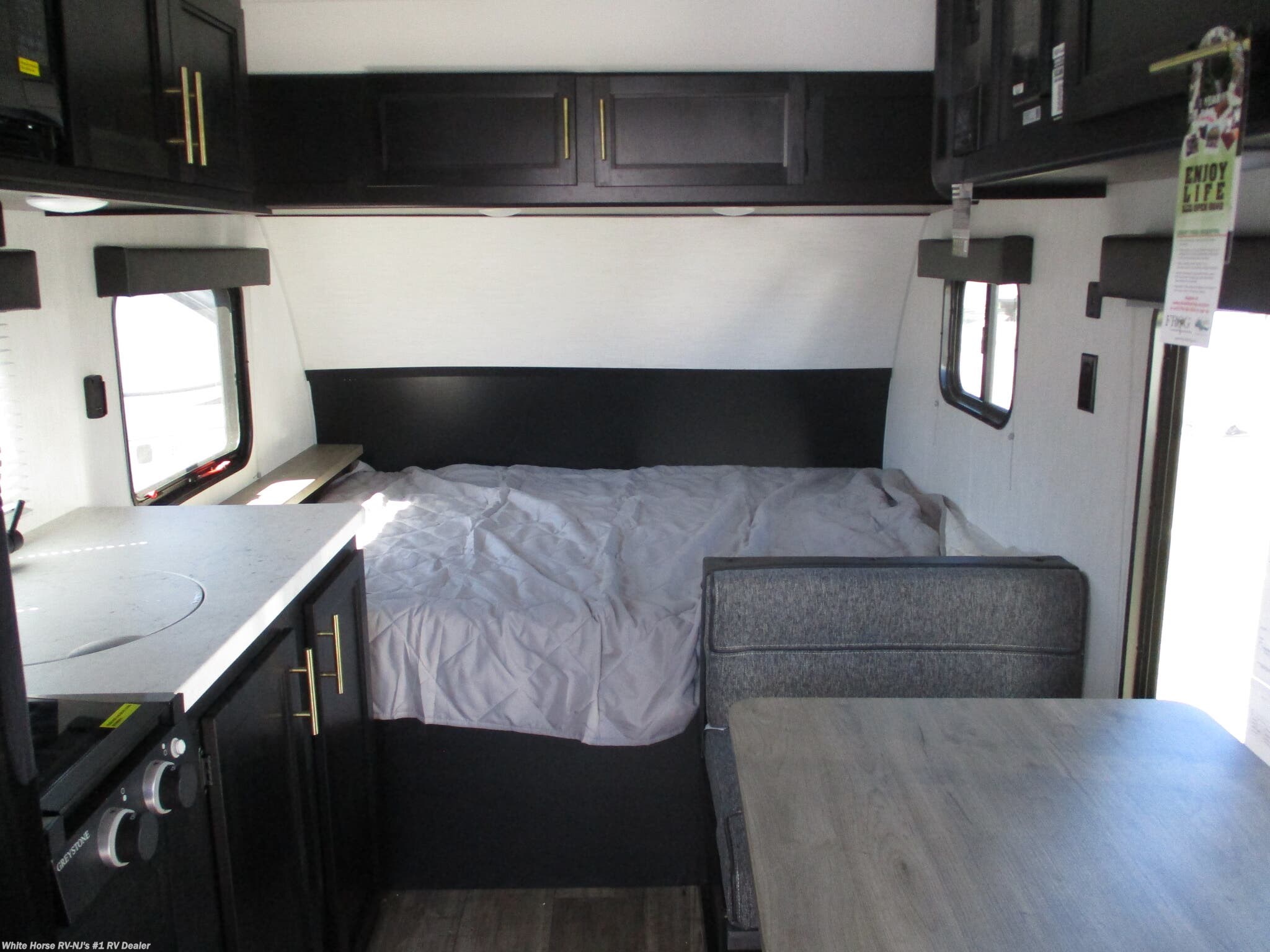Modern RV rental interior: A bed, kitchen with GreyStone stove, and dining booth. Black cabinets & light walls create a cozy space.. Forest River Cherokee Wolf Pup 2021