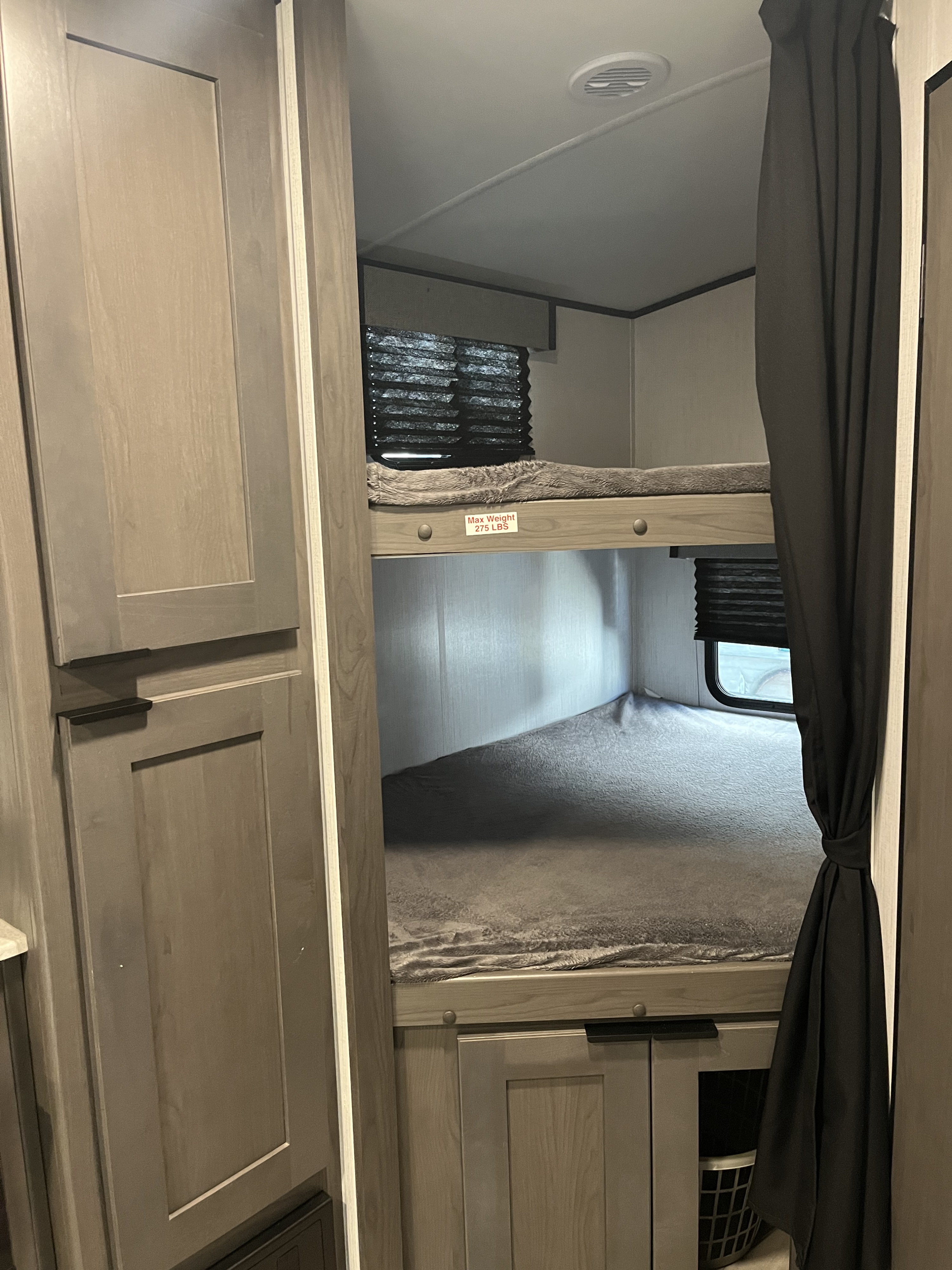 Cozy RV rental interior: two bunk beds with gray blankets, window, and cabinet storage. Upper bunk max weight 275 lbs.. Cruiser RV MPG Ultra Lite 2022