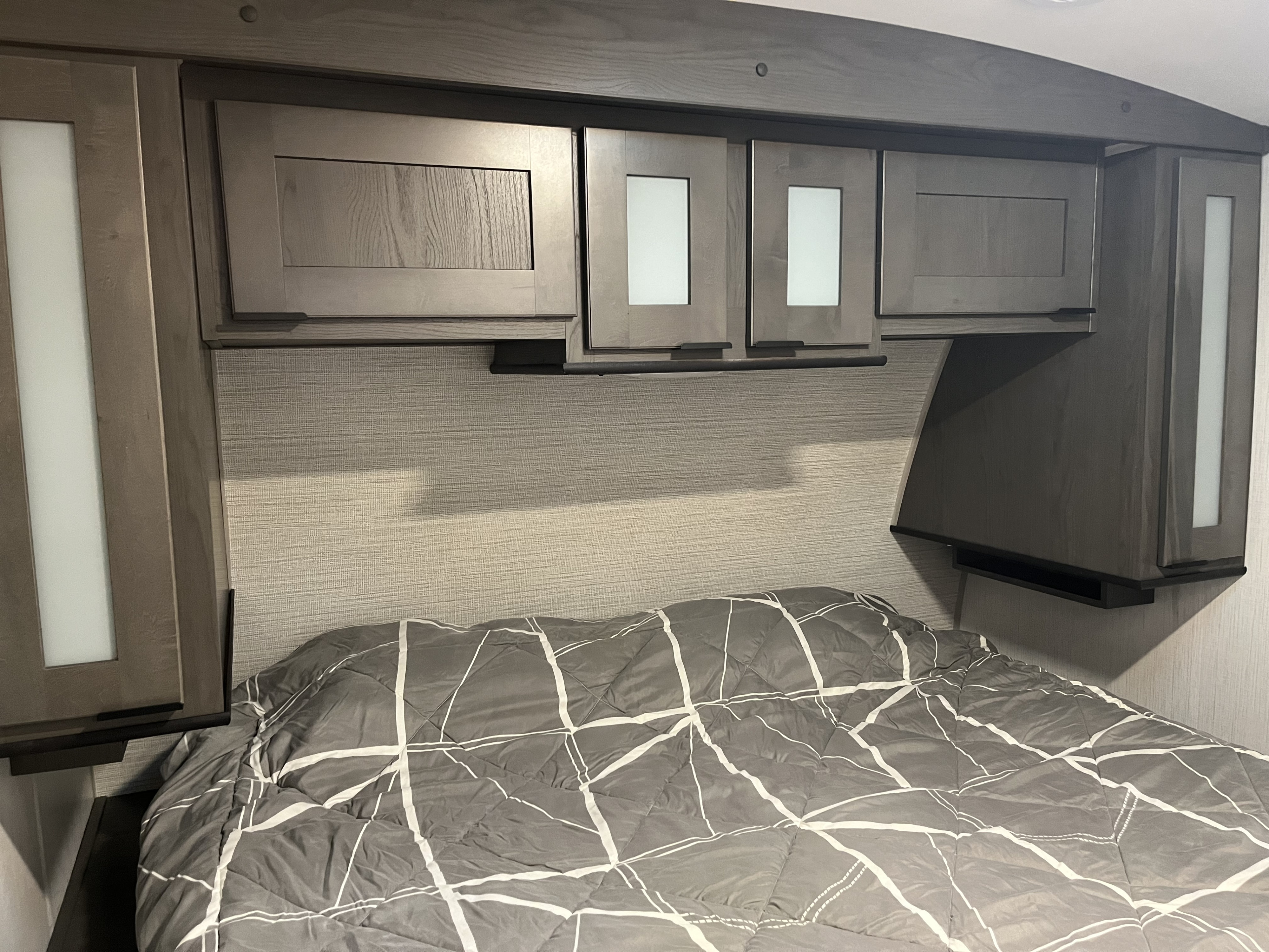 Inside this modern RV rental: a cozy bedroom with patterned bedding, ample overhead cabinets, and bedside storage.. Cruiser RV MPG Ultra Lite 2022