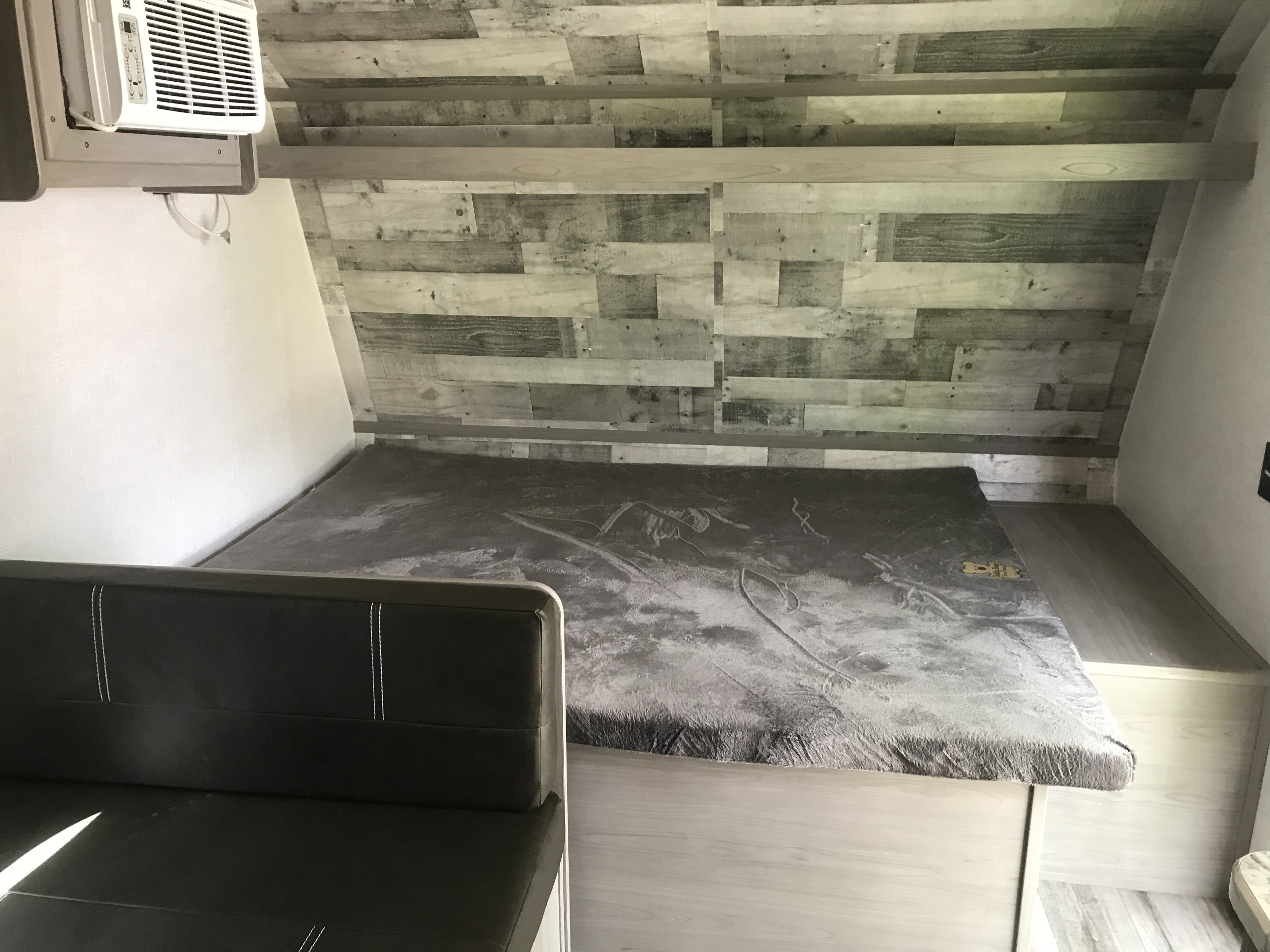 Compact RV rental sleeping area with textured blanket, comfy bench, and AC unit. Modern wood paneling adds a cozy feel.. Dutchmen Coleman Lantern 2023