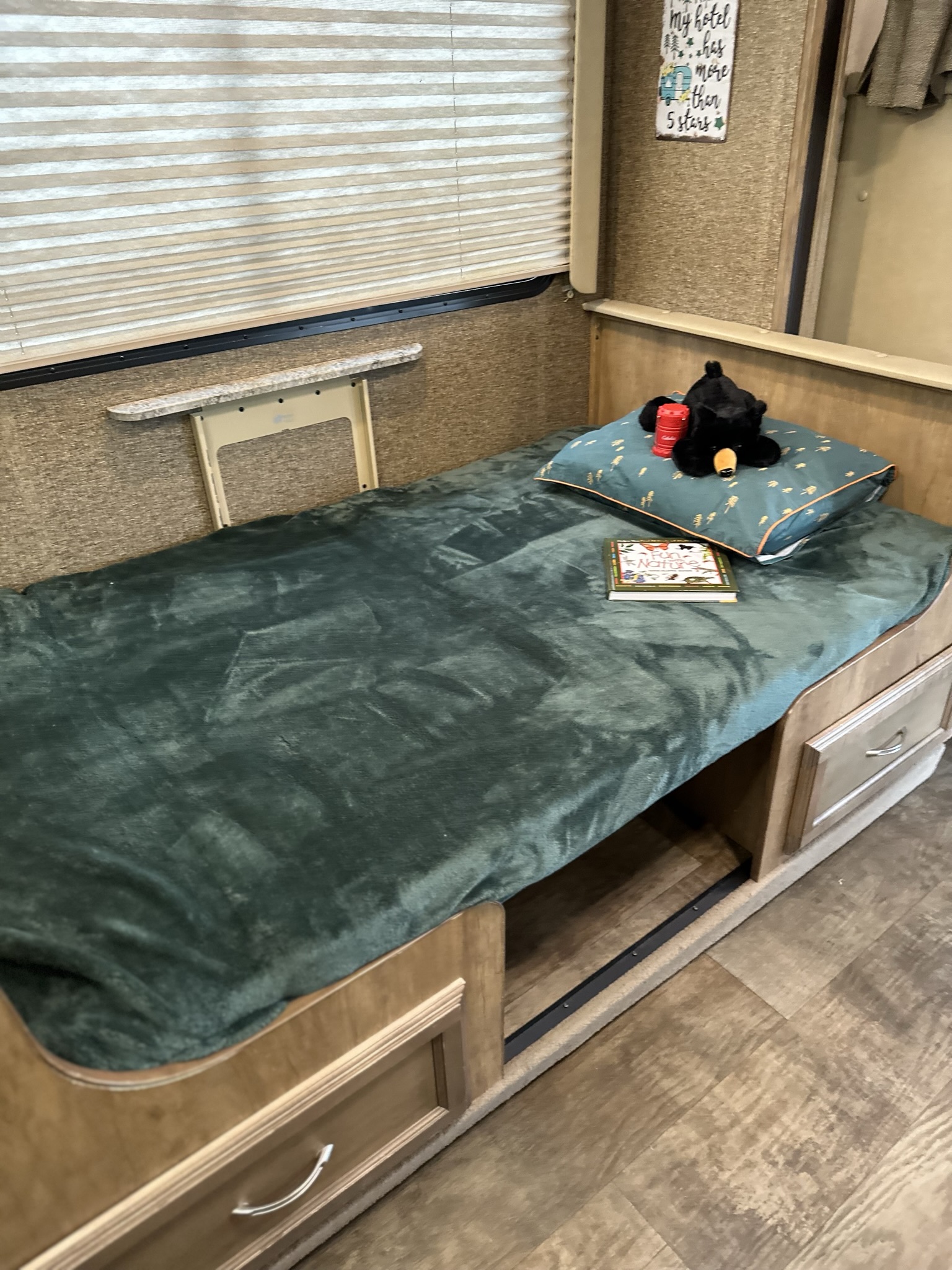 Interior of a cozy RV rental bedroom. Features include a bed with green blanket, pillow, bear plush, book, and convenient storage.. Gulf Stream Conquest 2017
